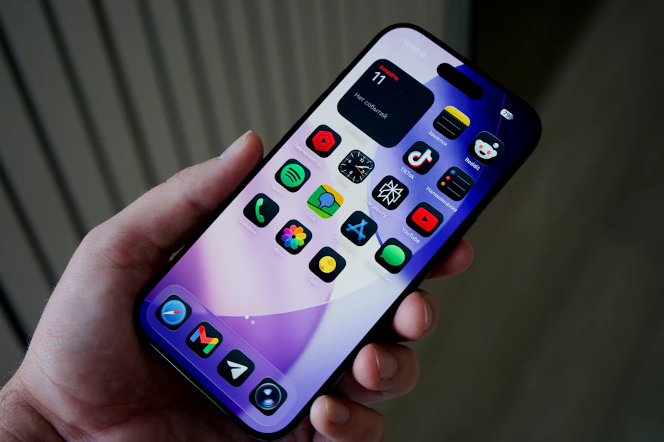 Hand holding a smartphone displaying a home screen full of colorful app icons, representing the apps Zapier connects together