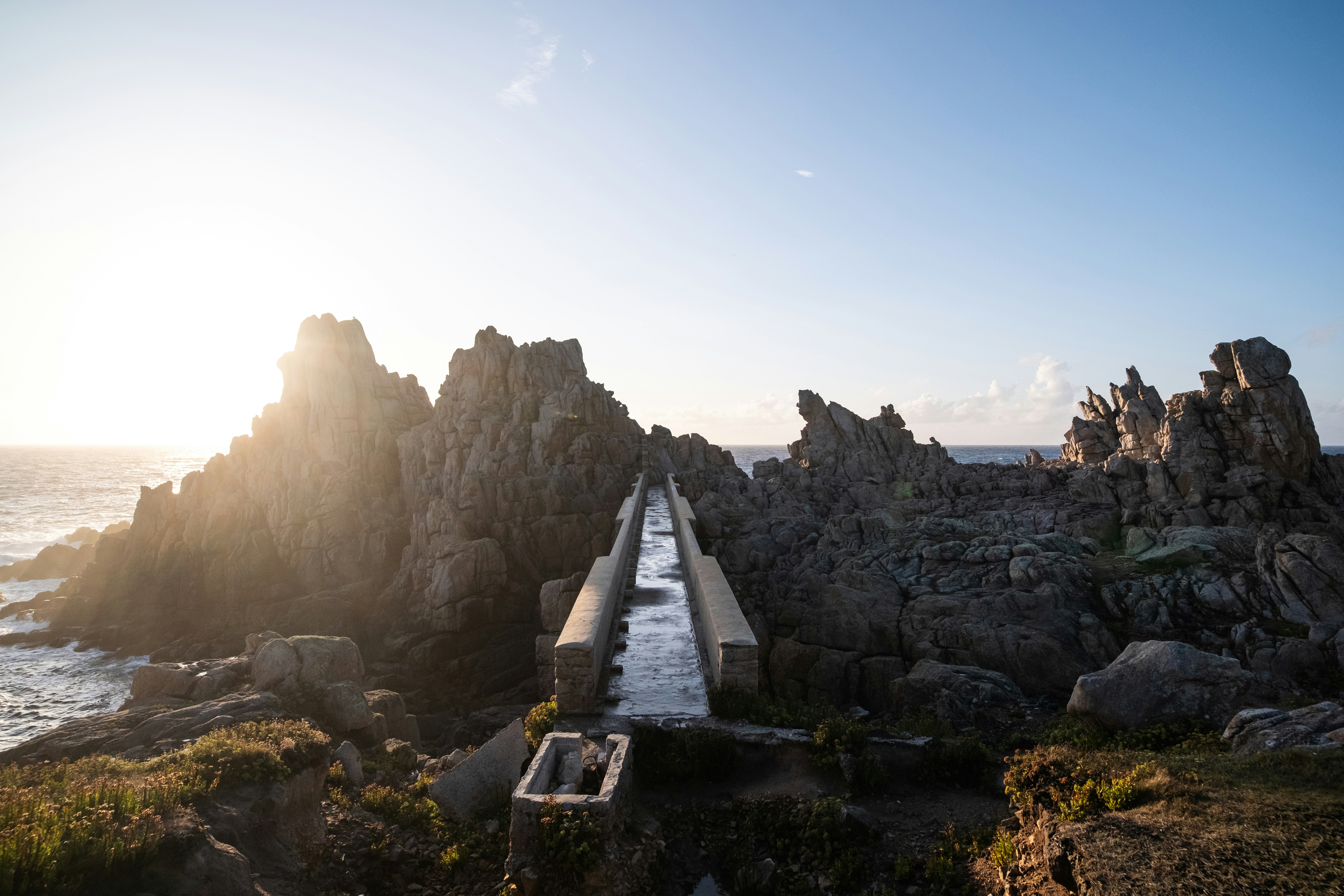 Una passerella di cemento conduce attraverso il paesaggio costiero roccioso al tramonto.