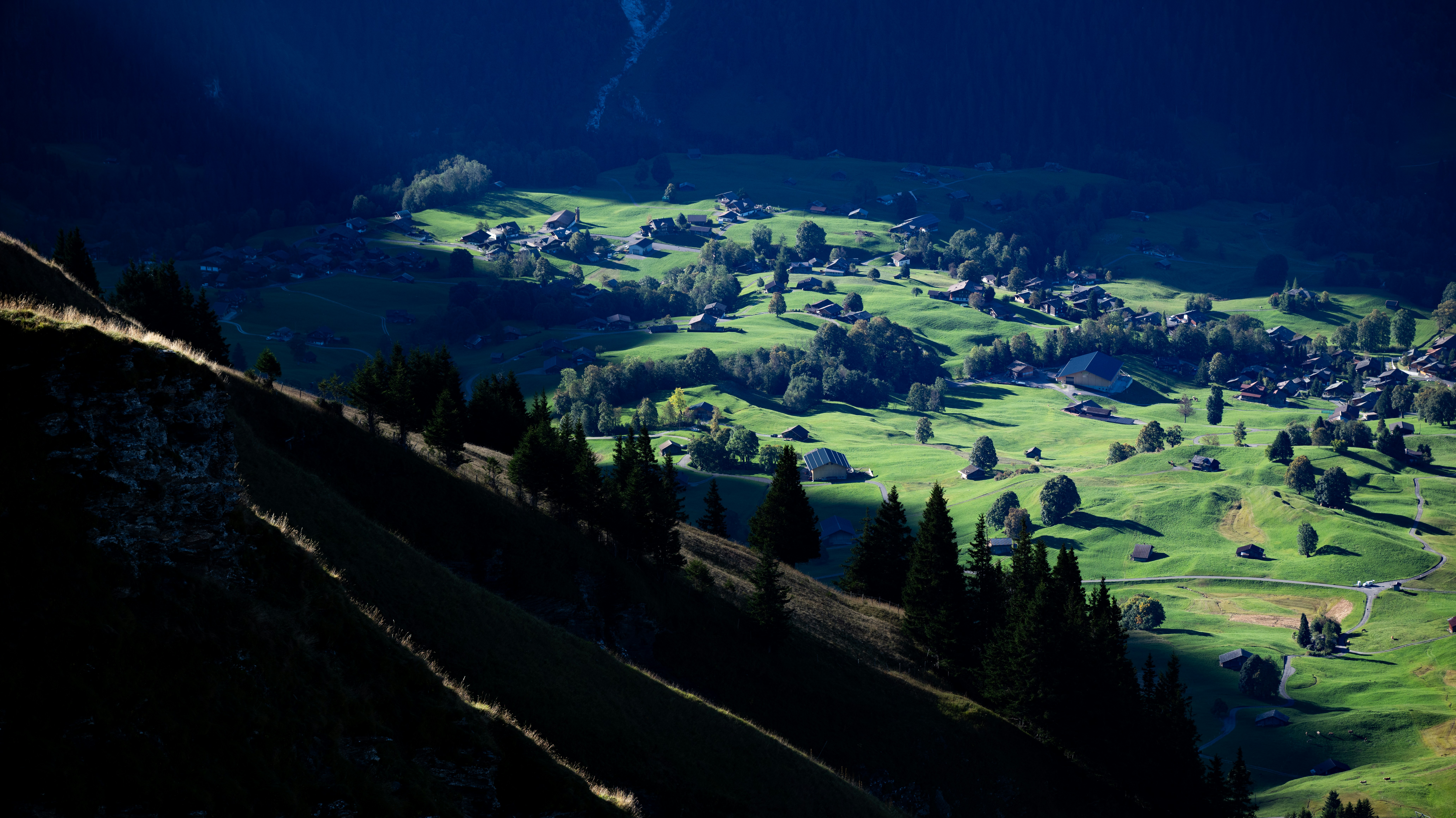 Sonnenbeschienenes Dorf, eingebettet in grüne sanfte Hügel.