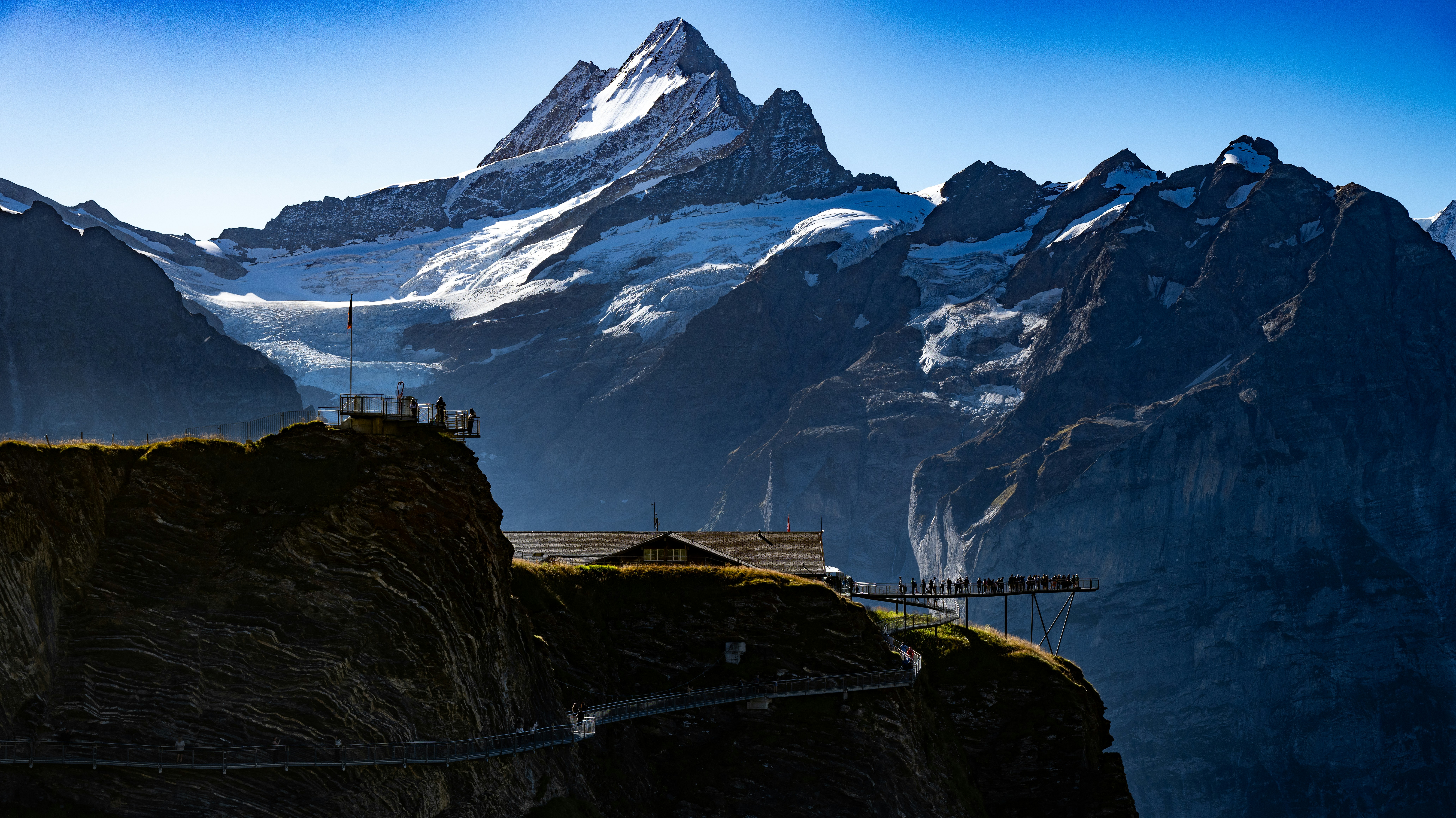 Snow-capped mountains rise behind a building on a cliff.