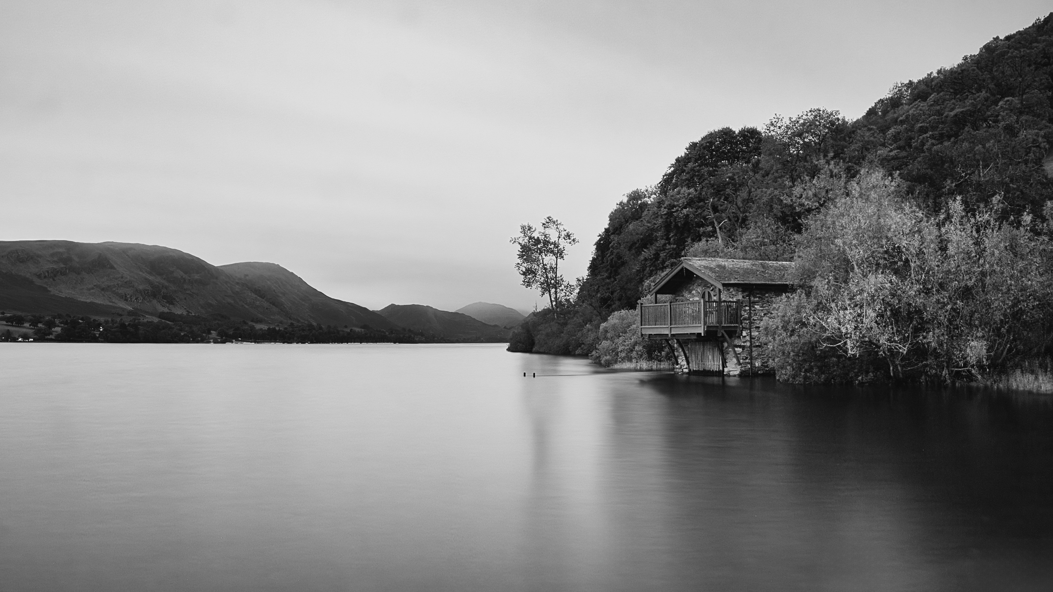 Rustic cabin by a calm lake with forested hills.