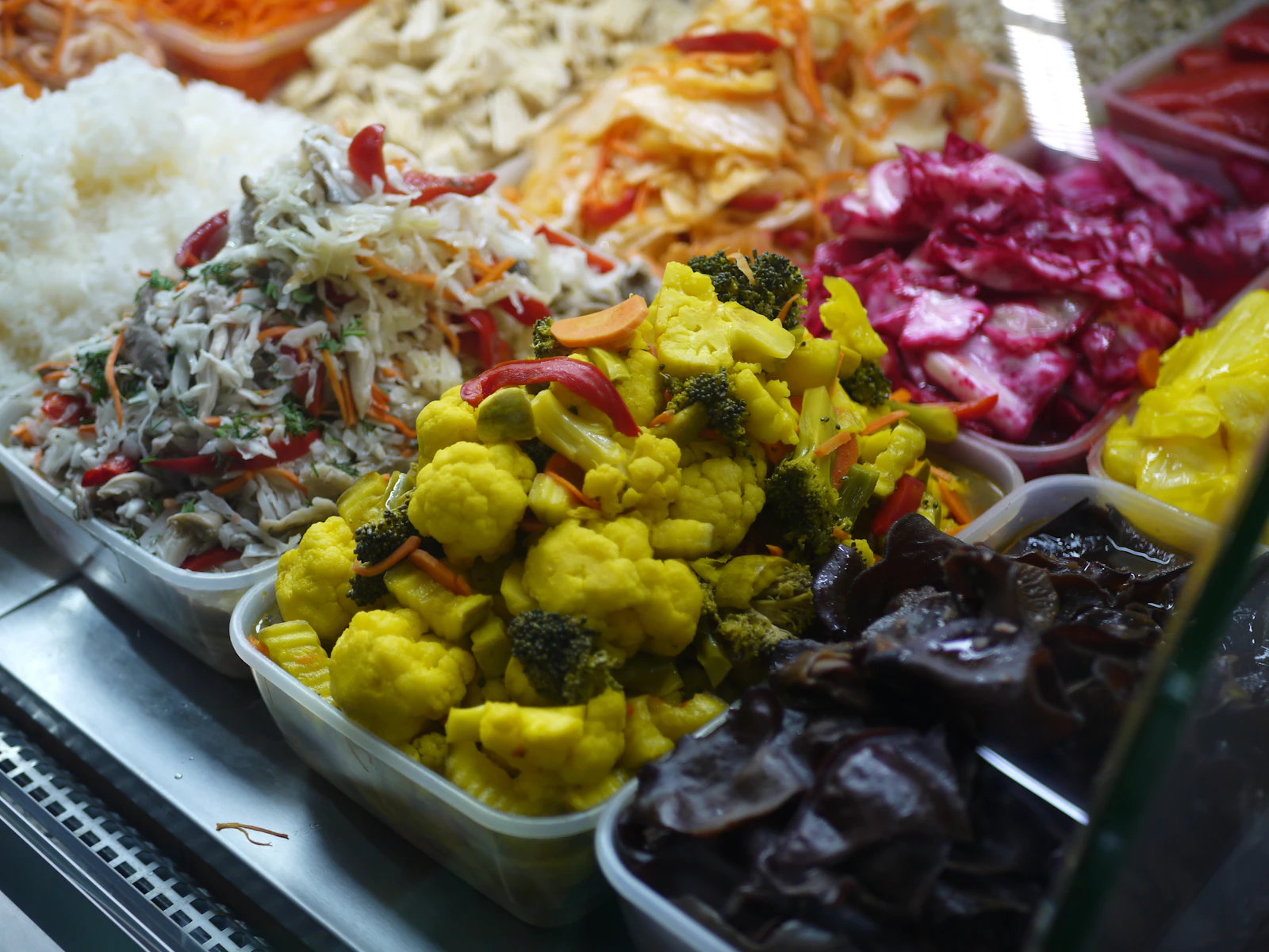 Illustrative image for vegan food in cairo: ful, taameya and koshari: Open containers filled with brightly coloured pickled cabbage, cauliflower, peppers and other vegetables.