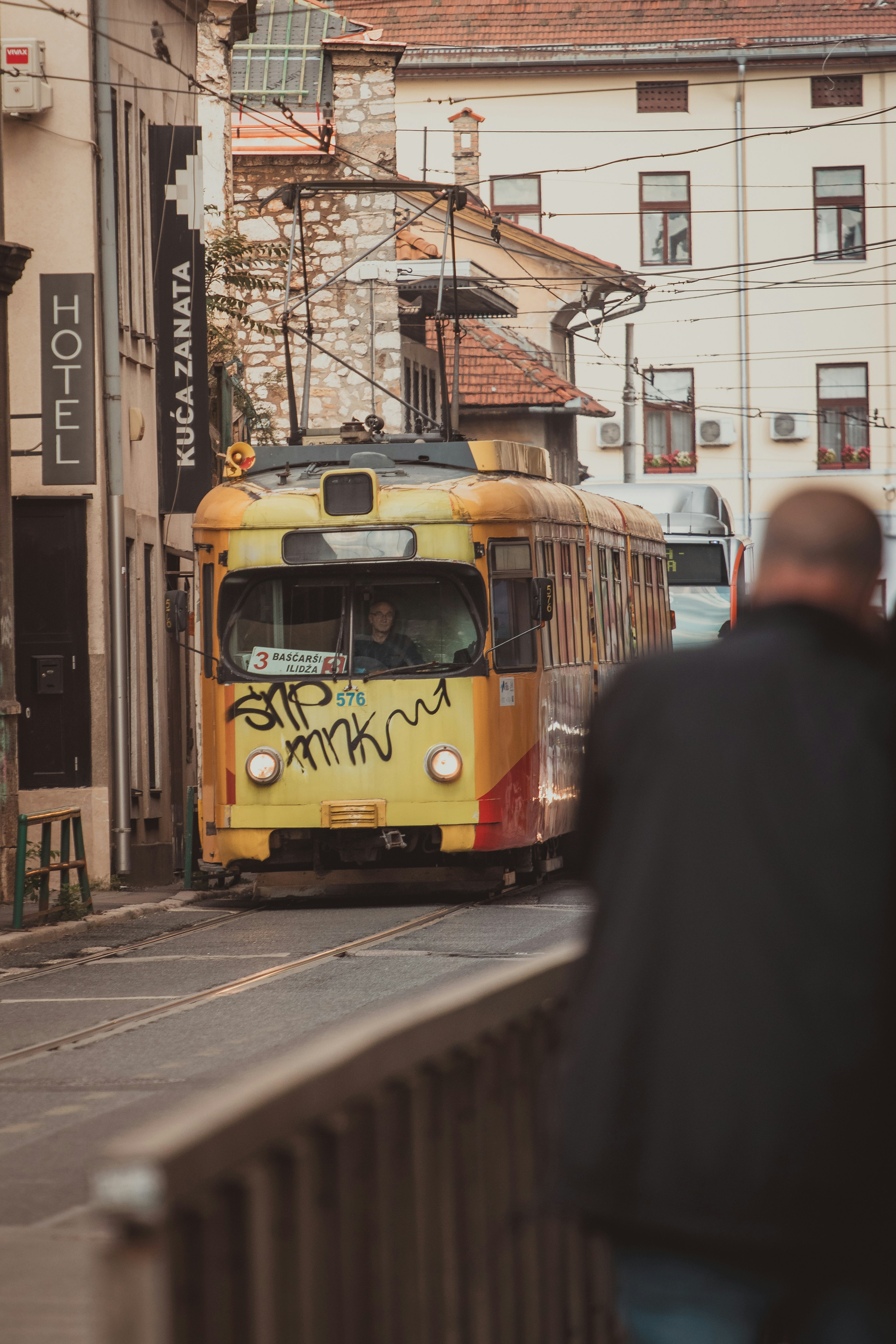 Yellow tram with graffiti on a city street.