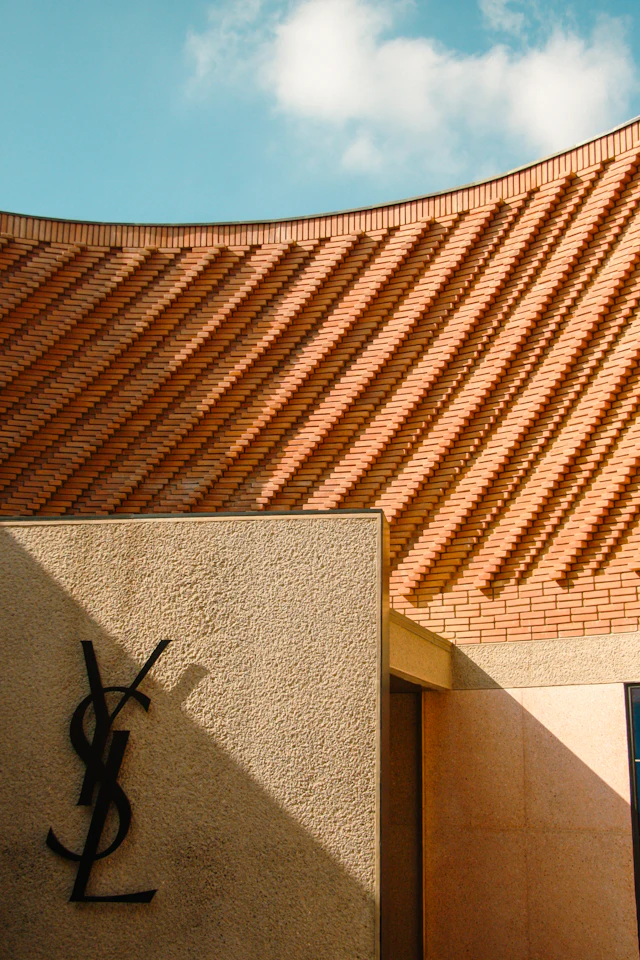 The YSL monogram sign against the museum's terracotta-brick wall under a blue sky.