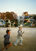 Children chase giant bubbles in a park.