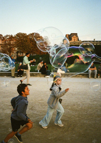Children chase giant bubbles in a park.