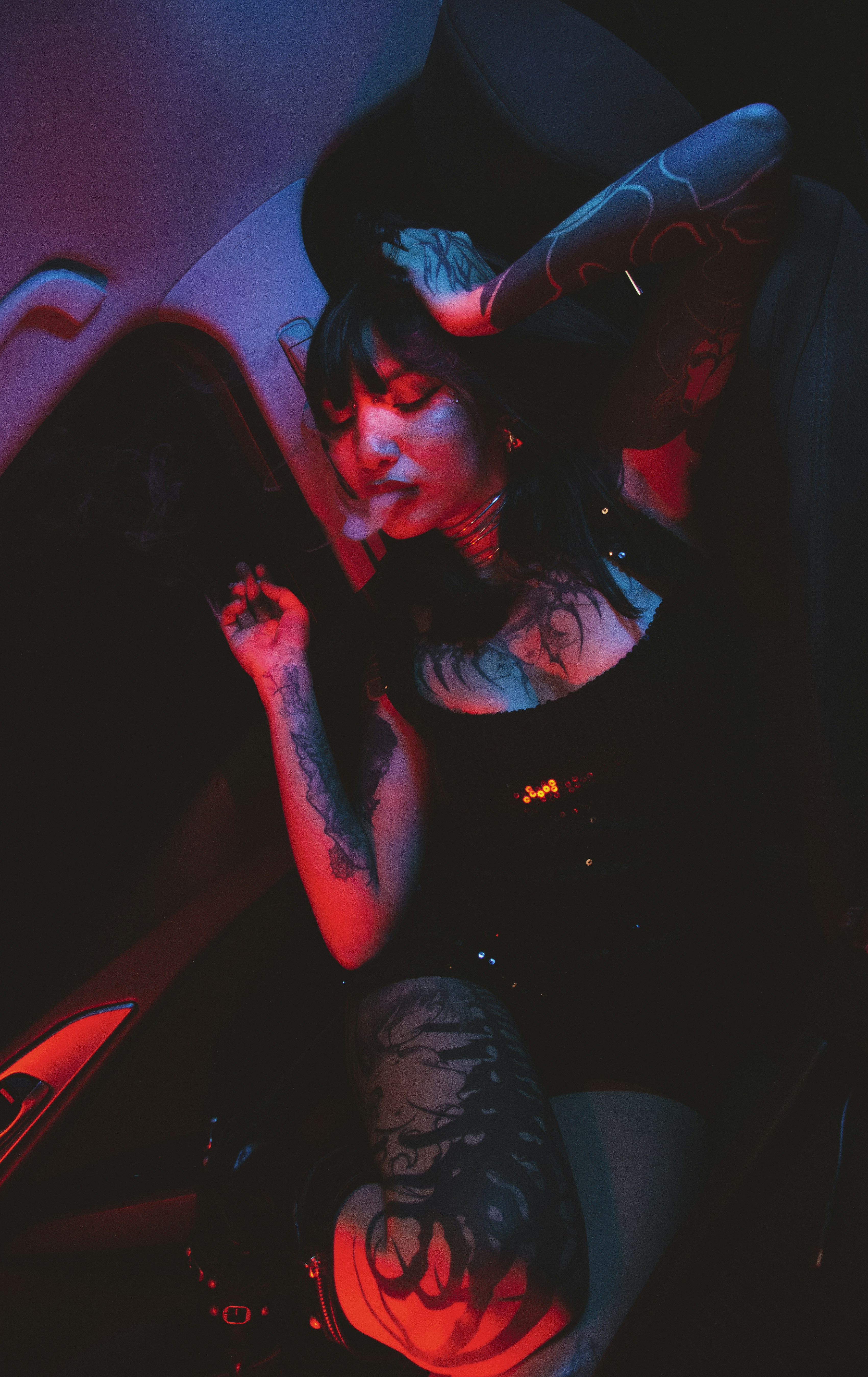 Woman with tattoos smoking in red and blue light