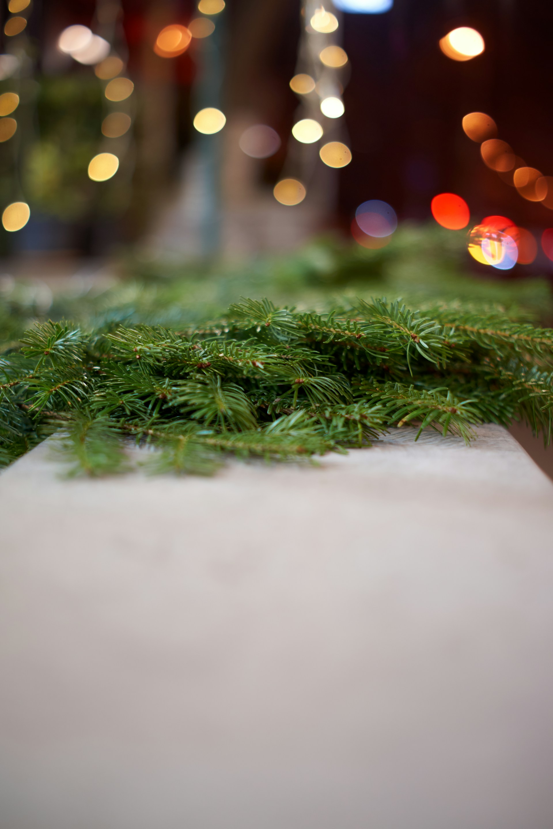 Green fir branches on a wooden surface with bokeh lights.