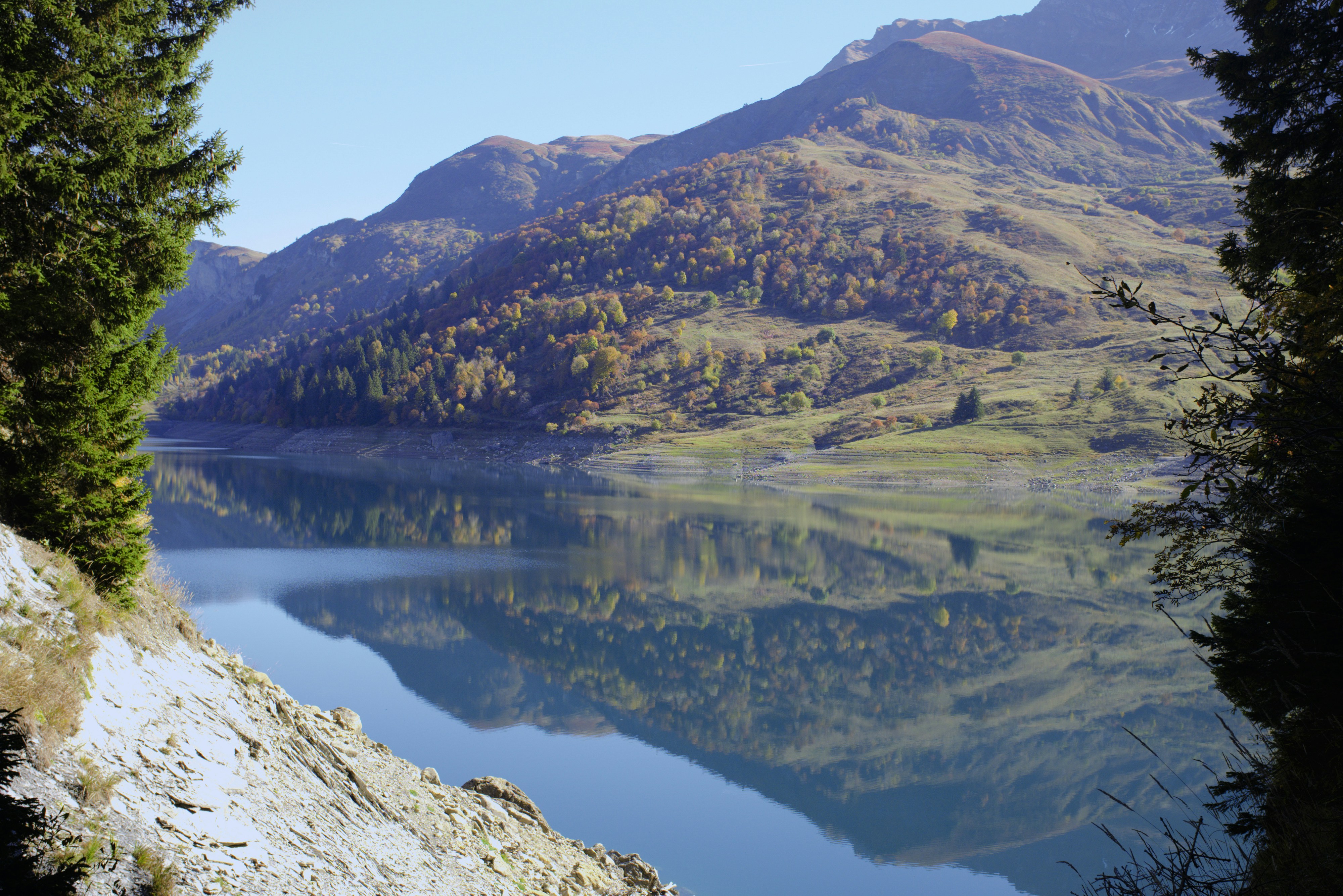 Le lac calme reflète les montagnes d’automne sous un ciel bleu clair.