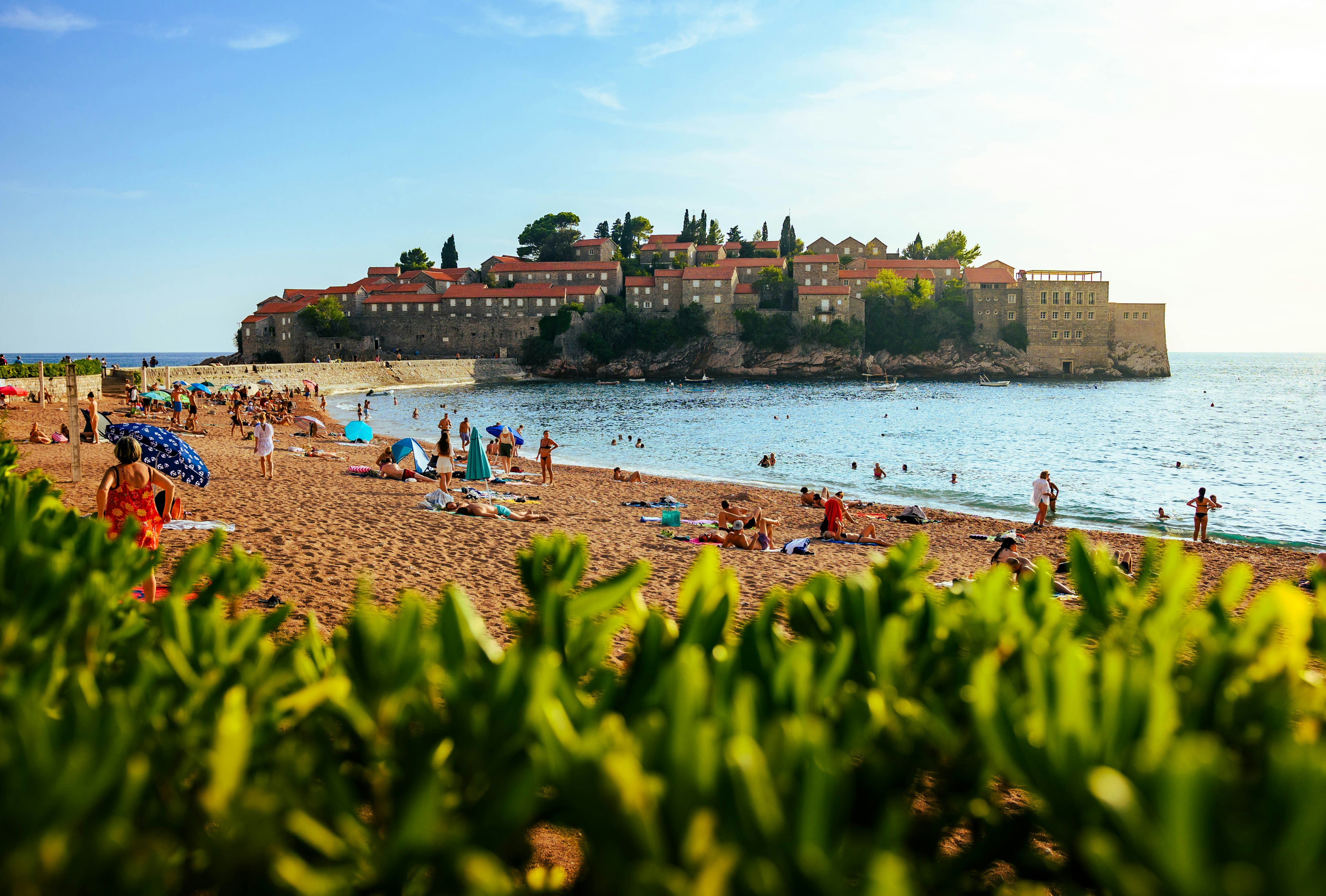 People relaxing on a sunny beach with island town offshore.