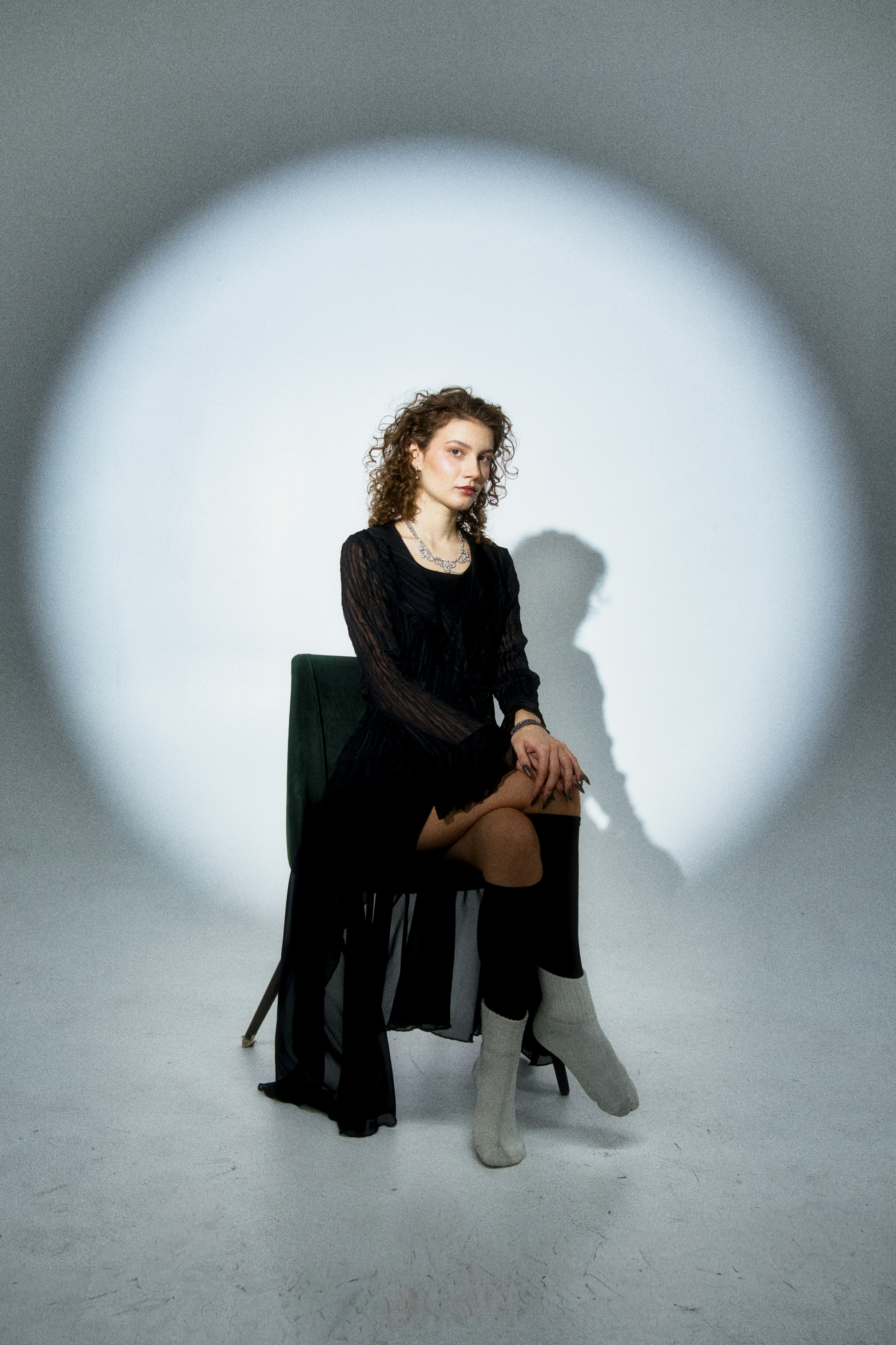 A young woman sits on a chair in a spotlight.