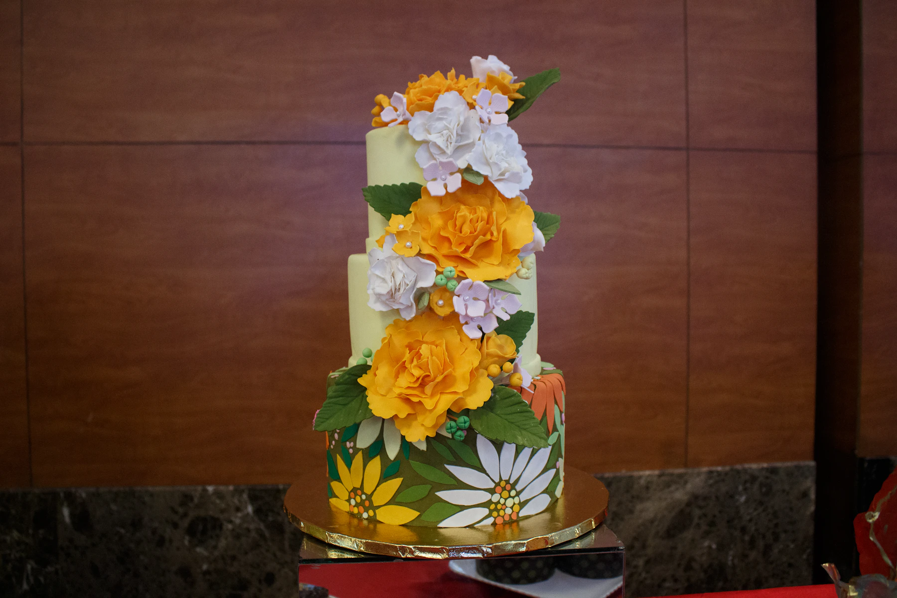 A three-tier fondant cake covered in handmade sugar roses, blossoms and daisies on a gold board