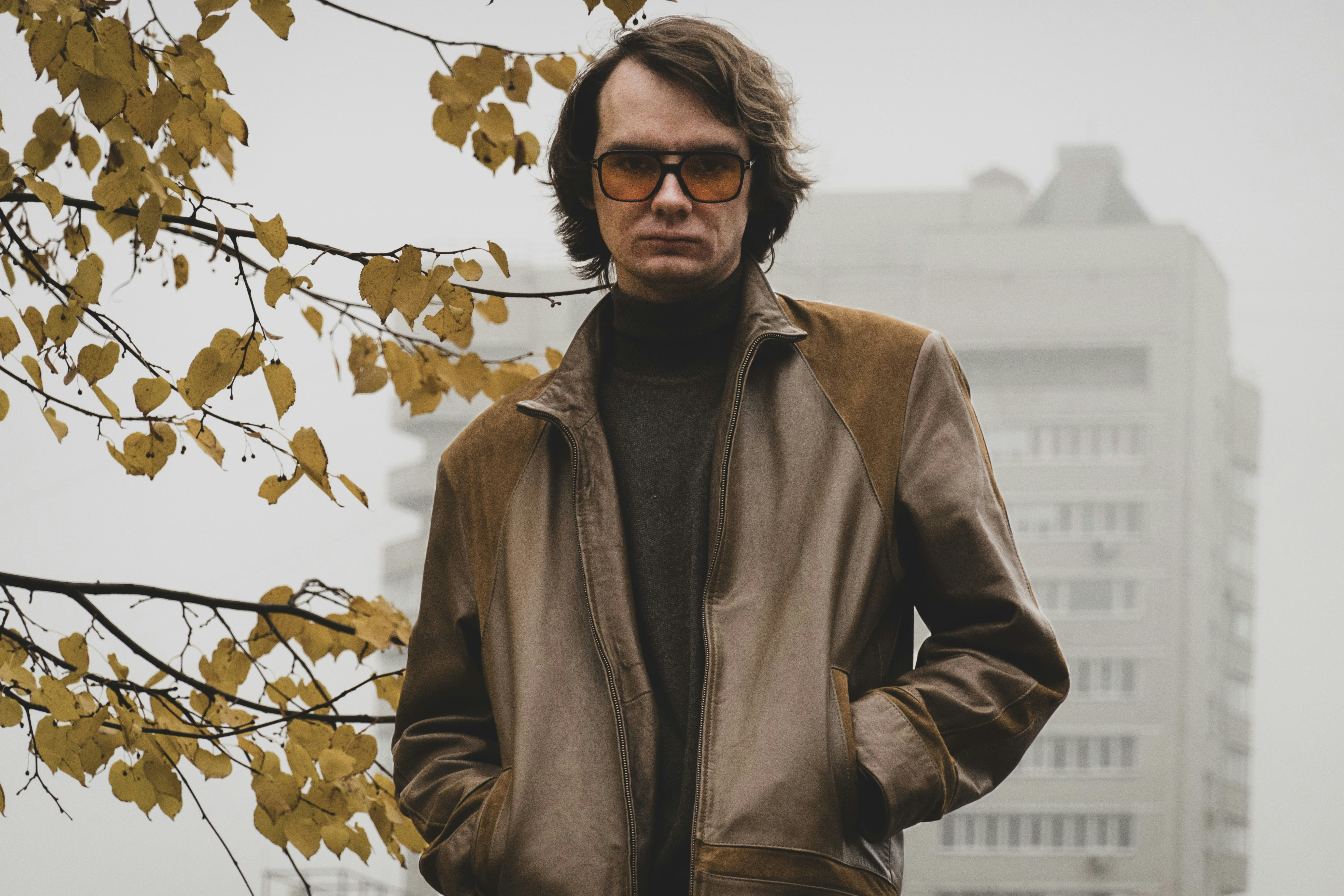 Man in brown jacket and turtleneck stands outside