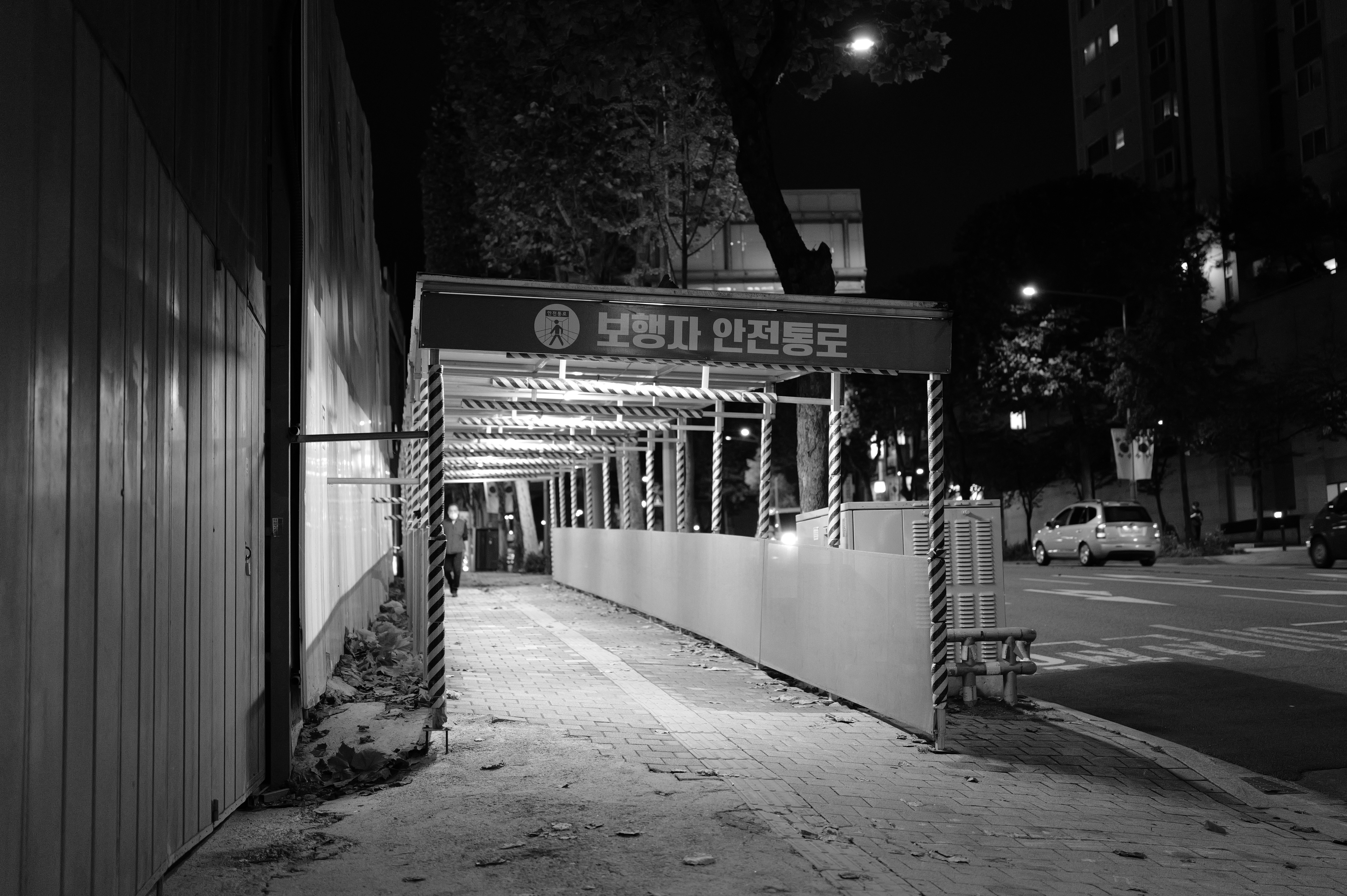 A covered walkway at night with cars in background