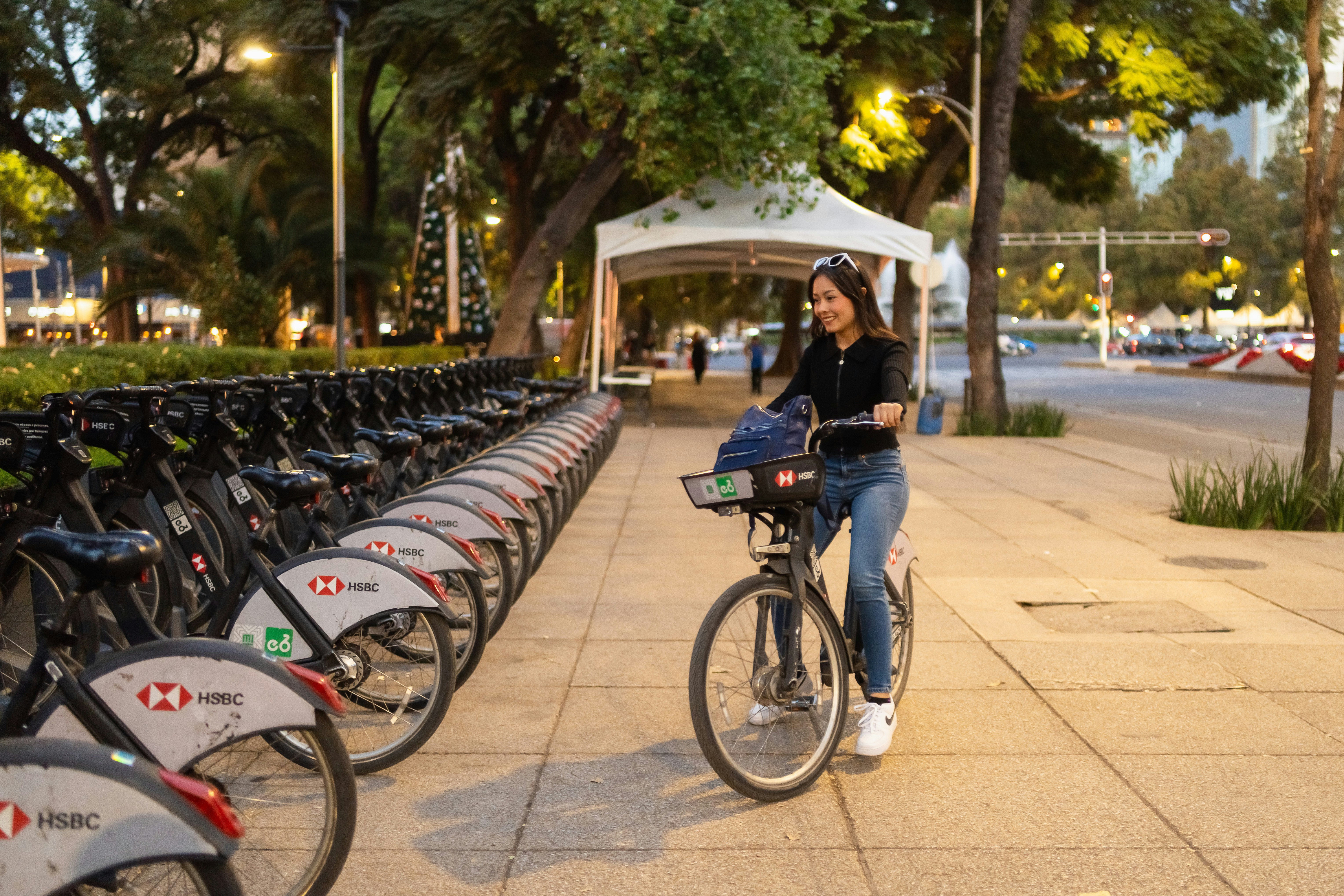 Woman walking a bicycle next to a row of bikes.