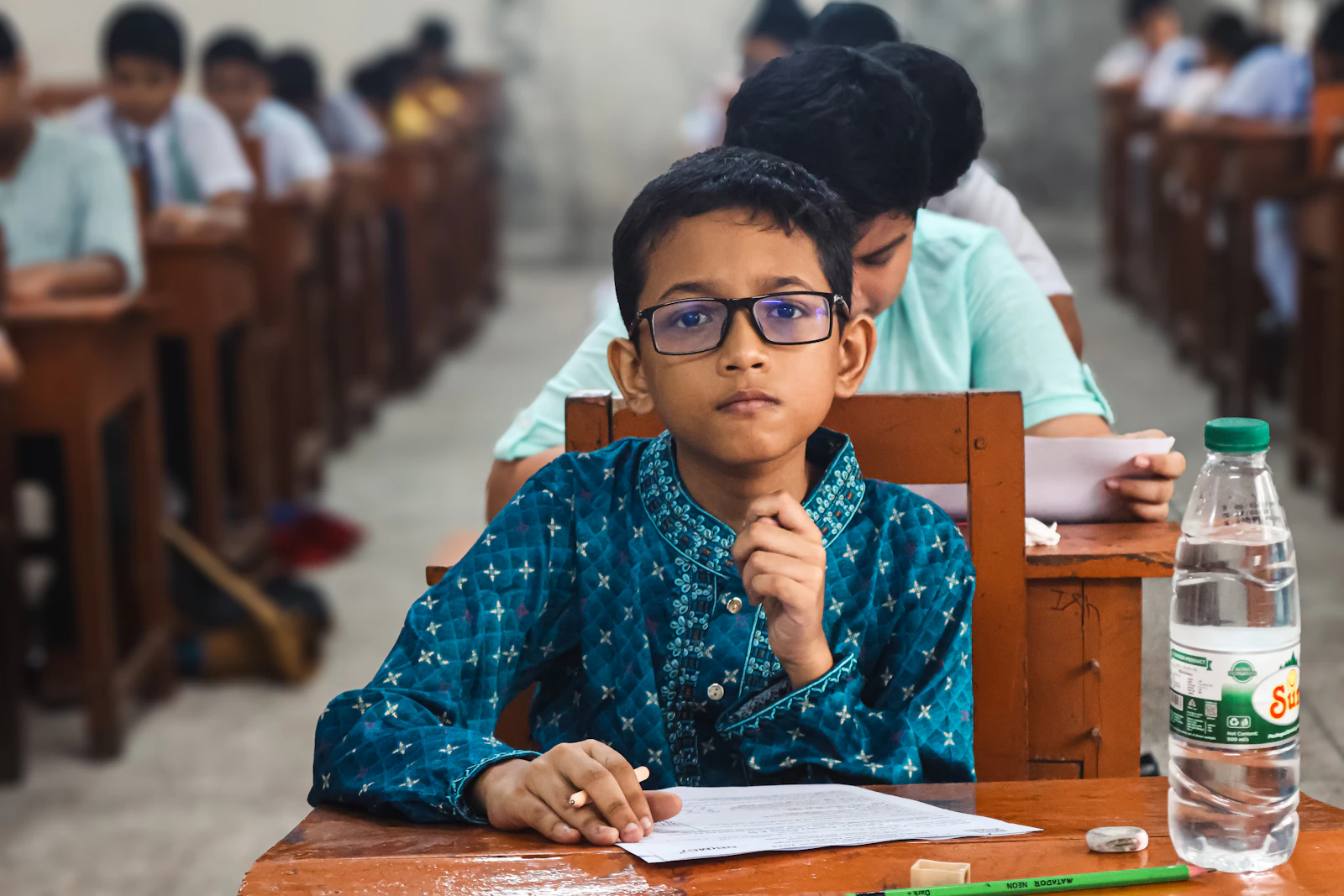 Student wearing glasses writing a test at a desk