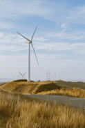 Wind turbines on a grassy hill under a blue sky.