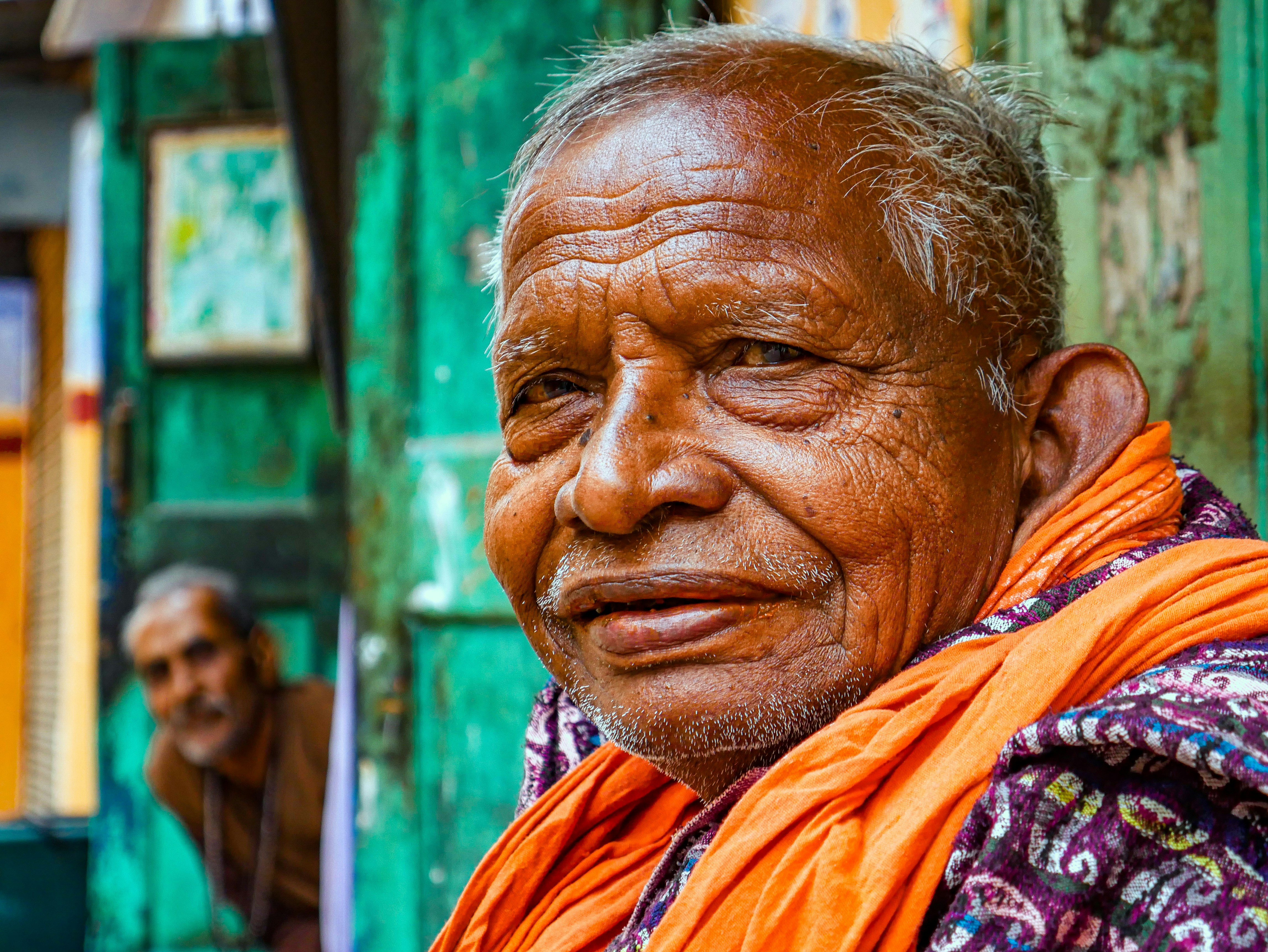 Elderly man with orange scarf smiles warmly smiles