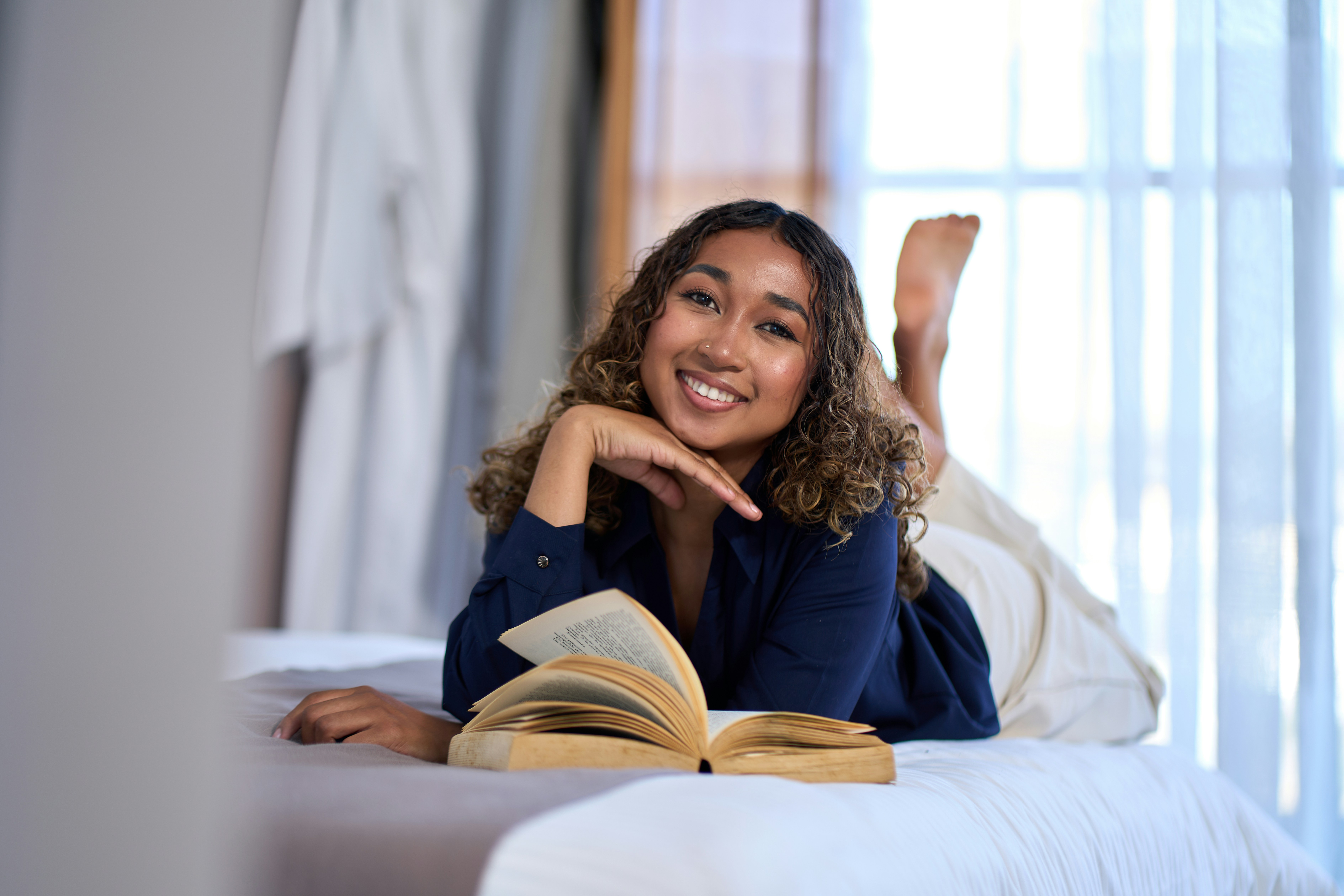 Young woman smiling while reading a book on bed