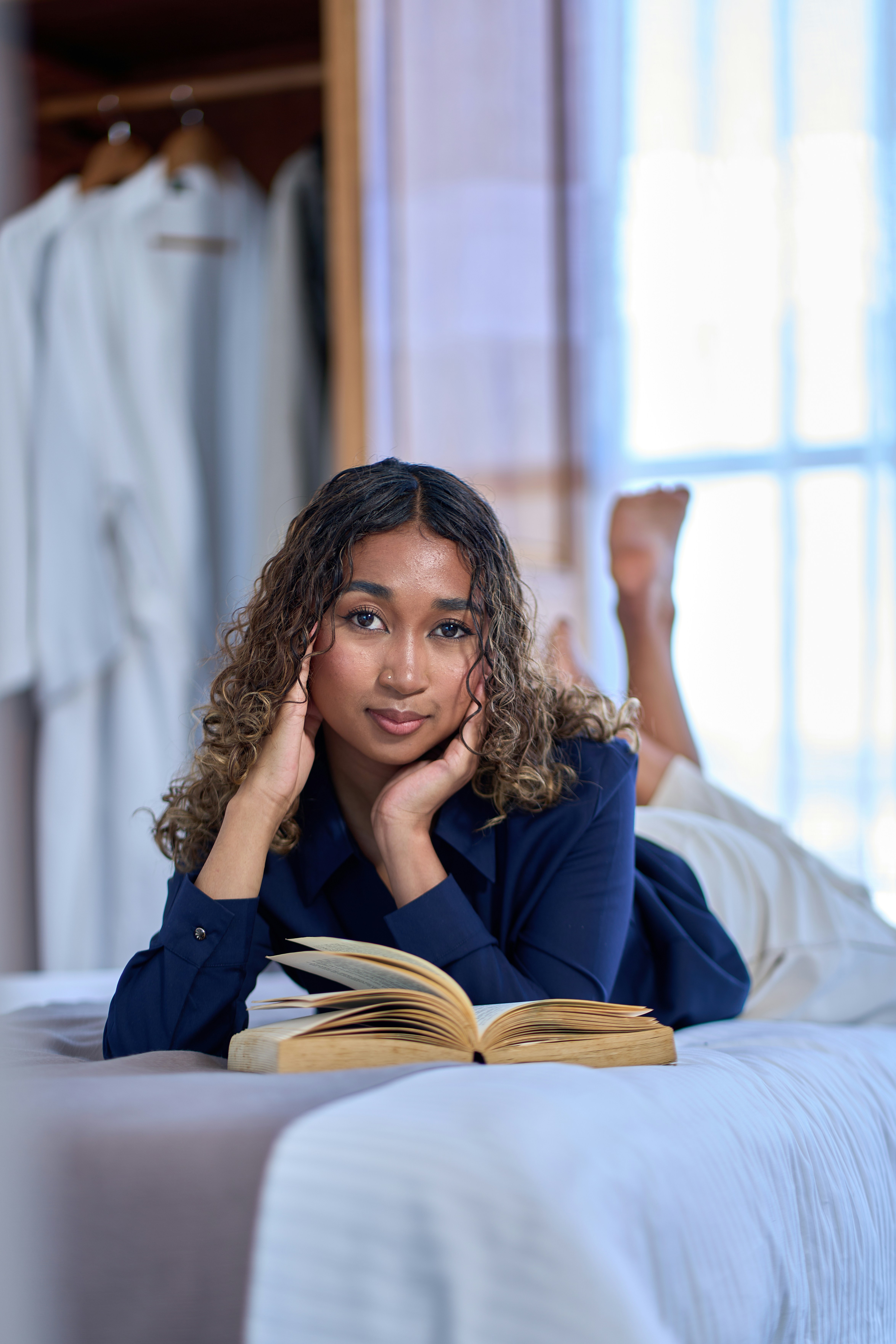 A young woman reads a book on a bed.