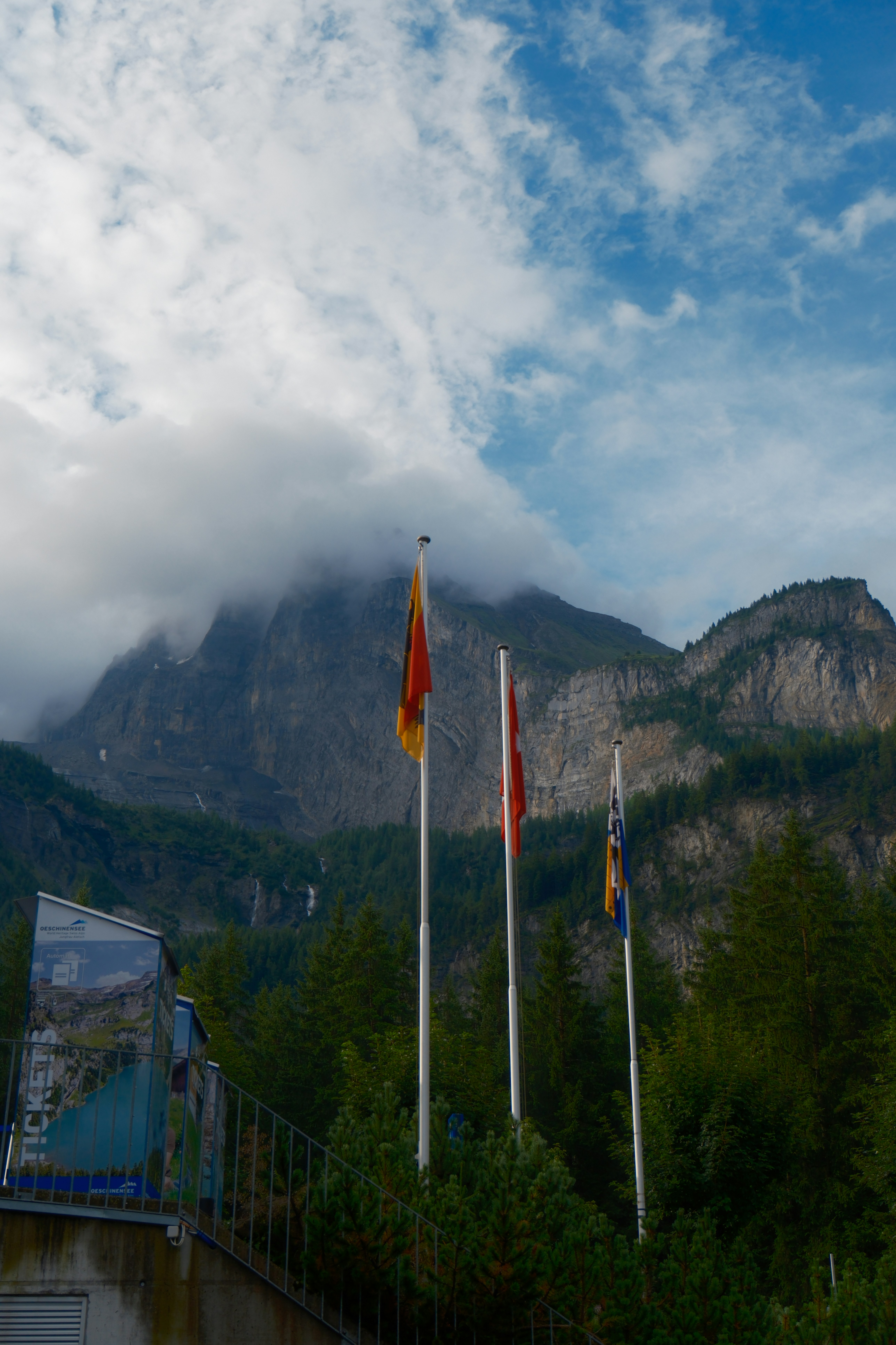 Flags fly before a cloudy mountain landscape.