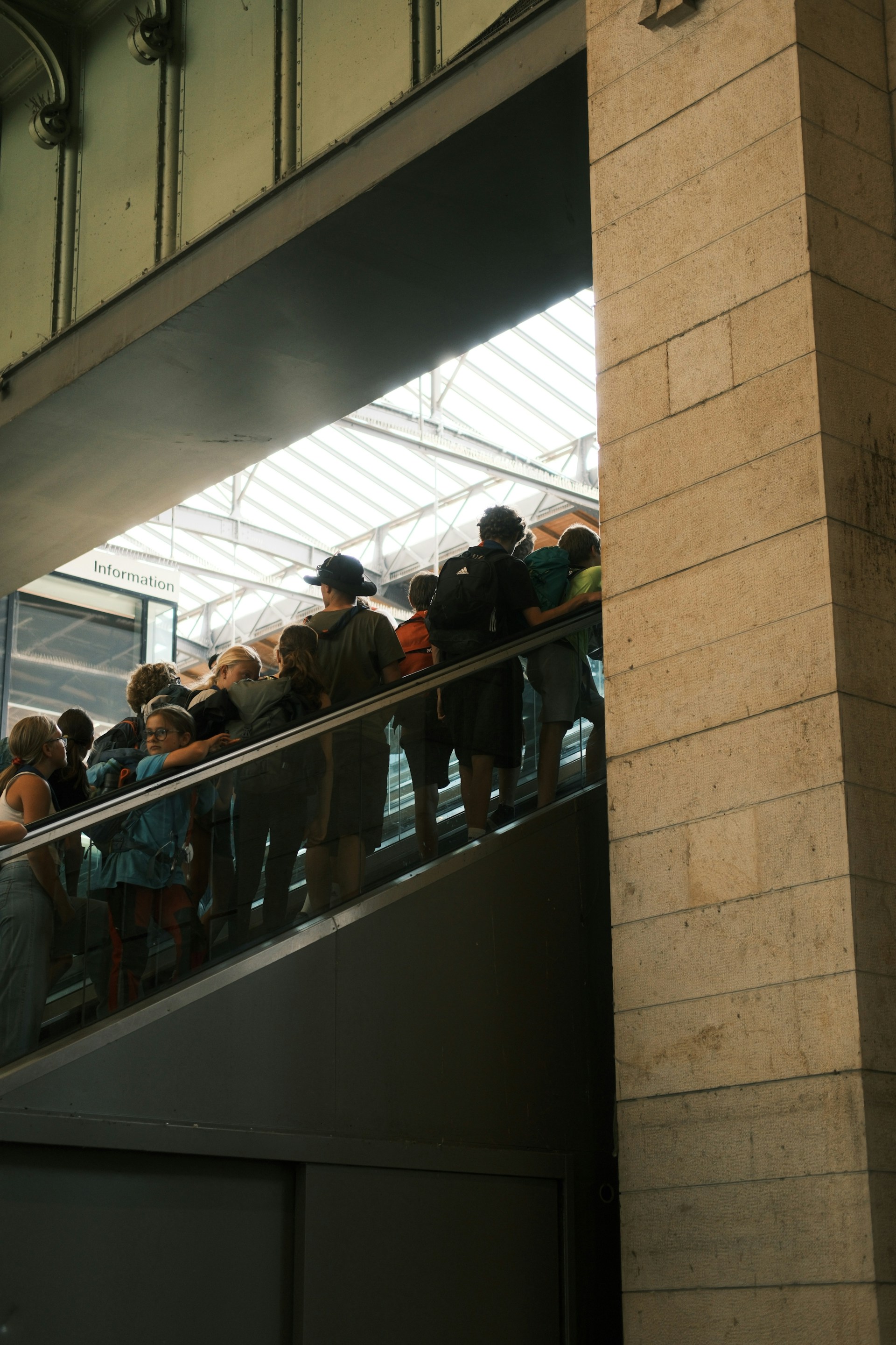 People riding an escalator upwards towards natural light