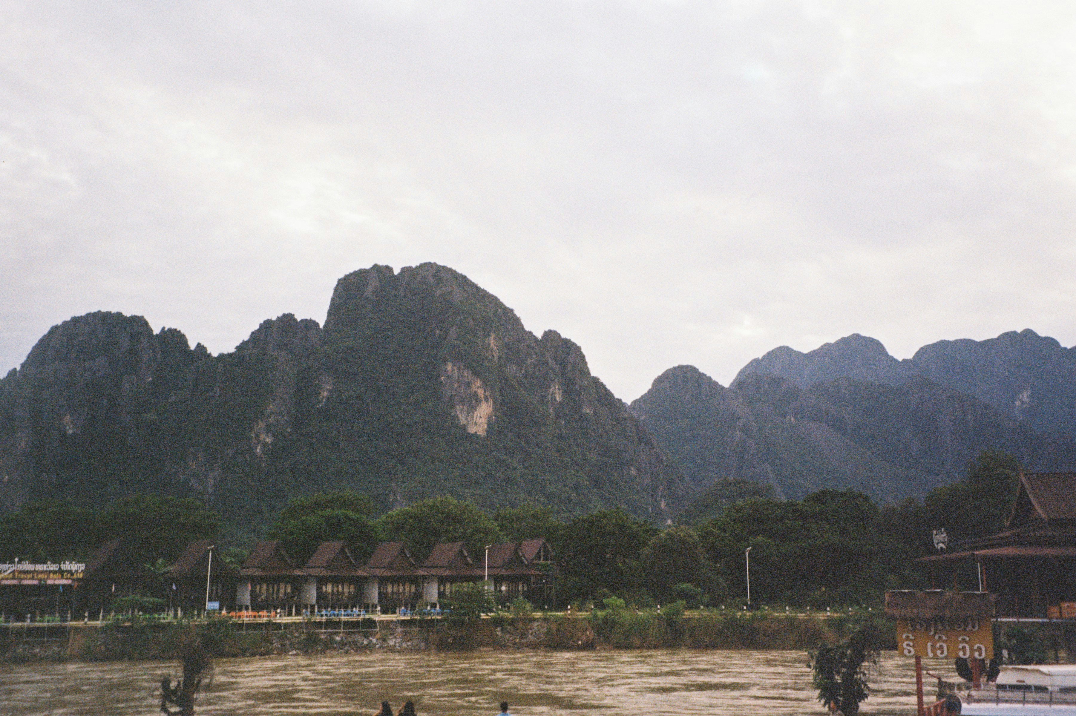 Jagged mountains rise behind lush green trees and buildings.