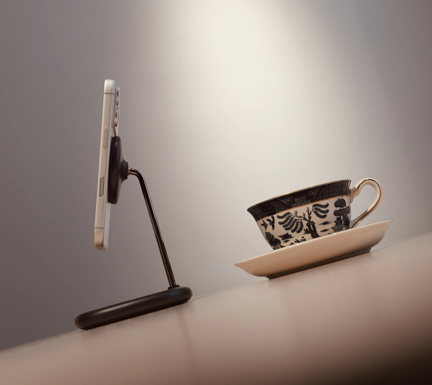 A phone held sideways on the Desk Stand beside a patterned teacup