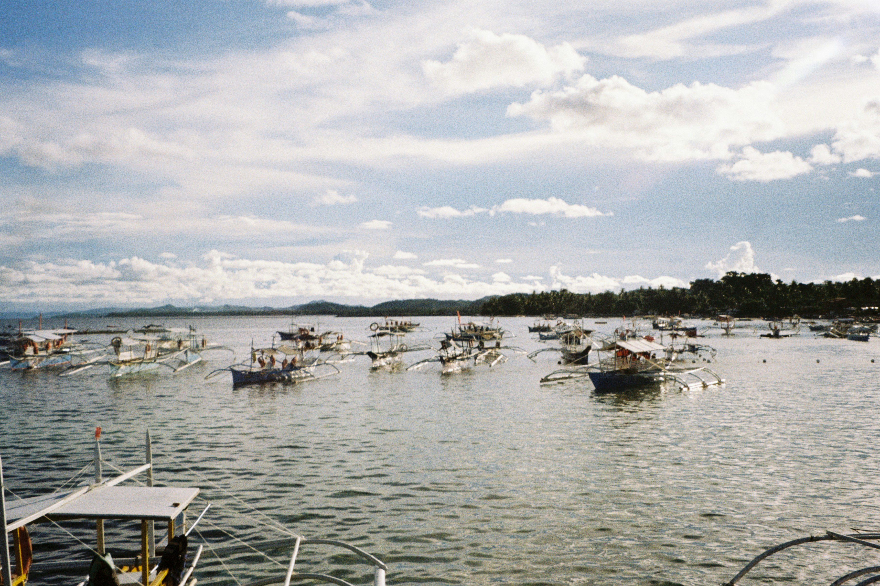 Many boats anchored in a calm bay under clouds.