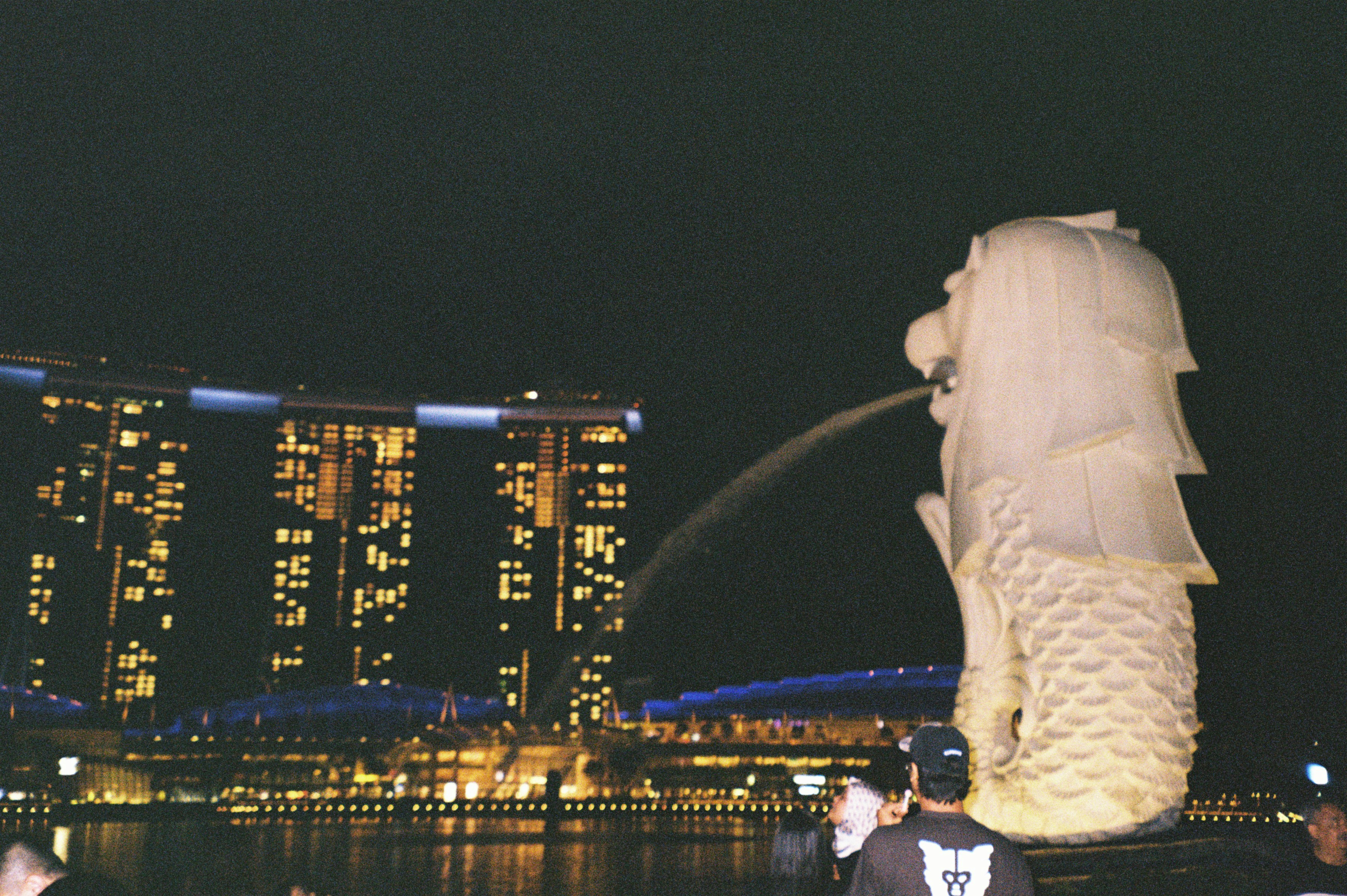 Merlion statue spouting water with city skyline at night