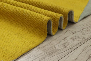 Yellow textured rug folded over wooden floor