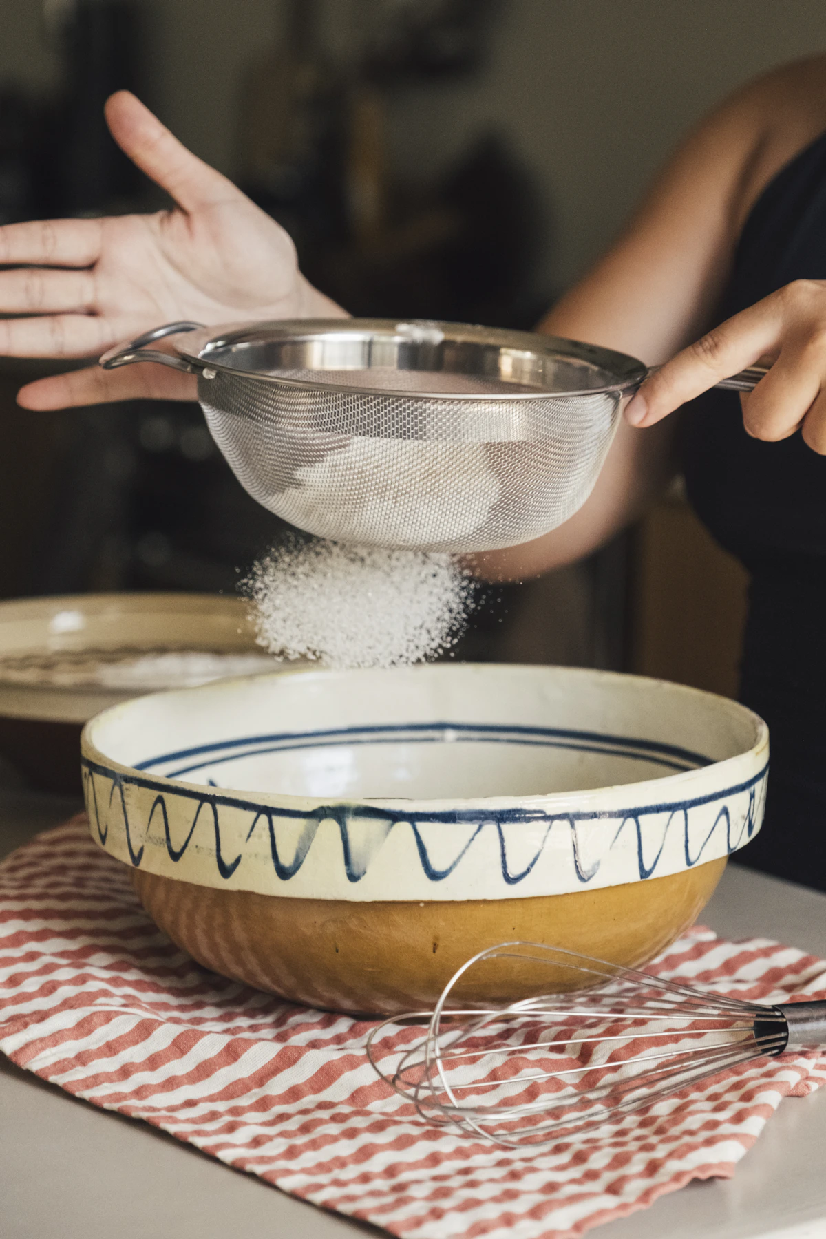 Flour being sifted through a fine sieve into a bowl, analogous to a graded screen where a coarse, cheap pass catches the obvious lumps before anything reaches a finer and more expensive stage