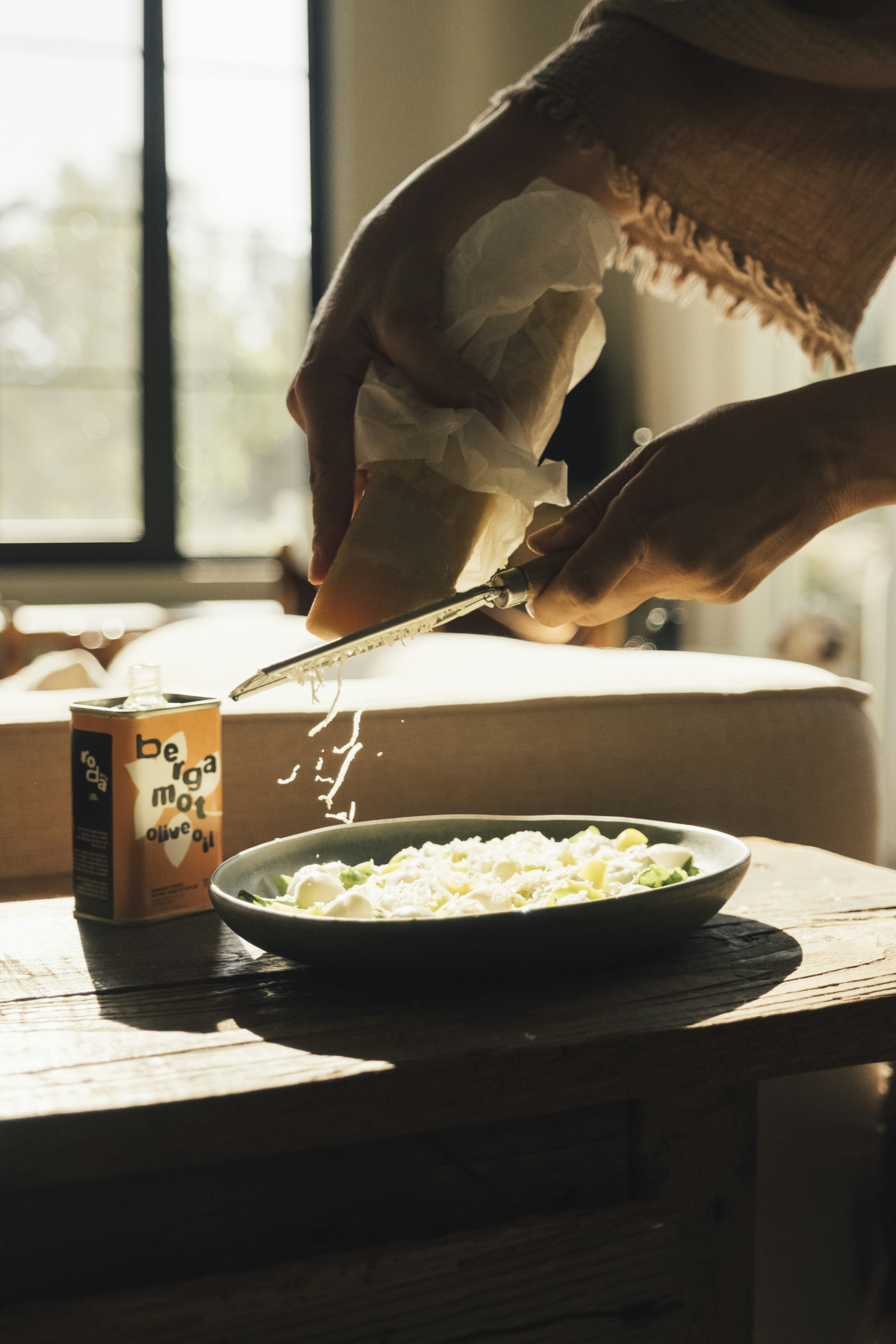 Hands grating cheese over a bowl of food.