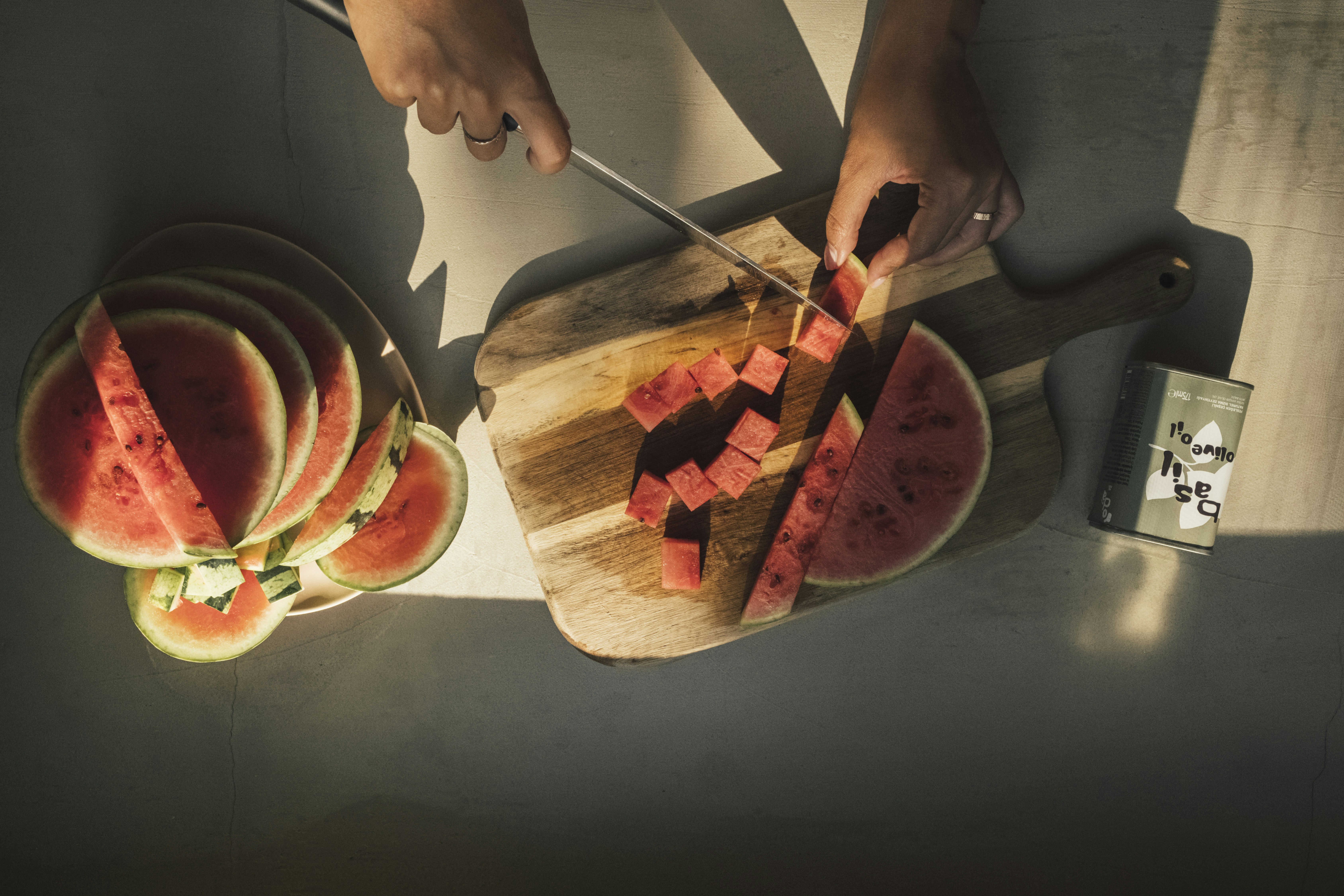 Manos cortando sandía en rodajas en una tabla de cortar de madera.