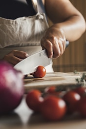 A person chopping a tomato on a cutting board.
