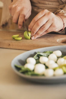 Hands chopping small green fruit on cutting board