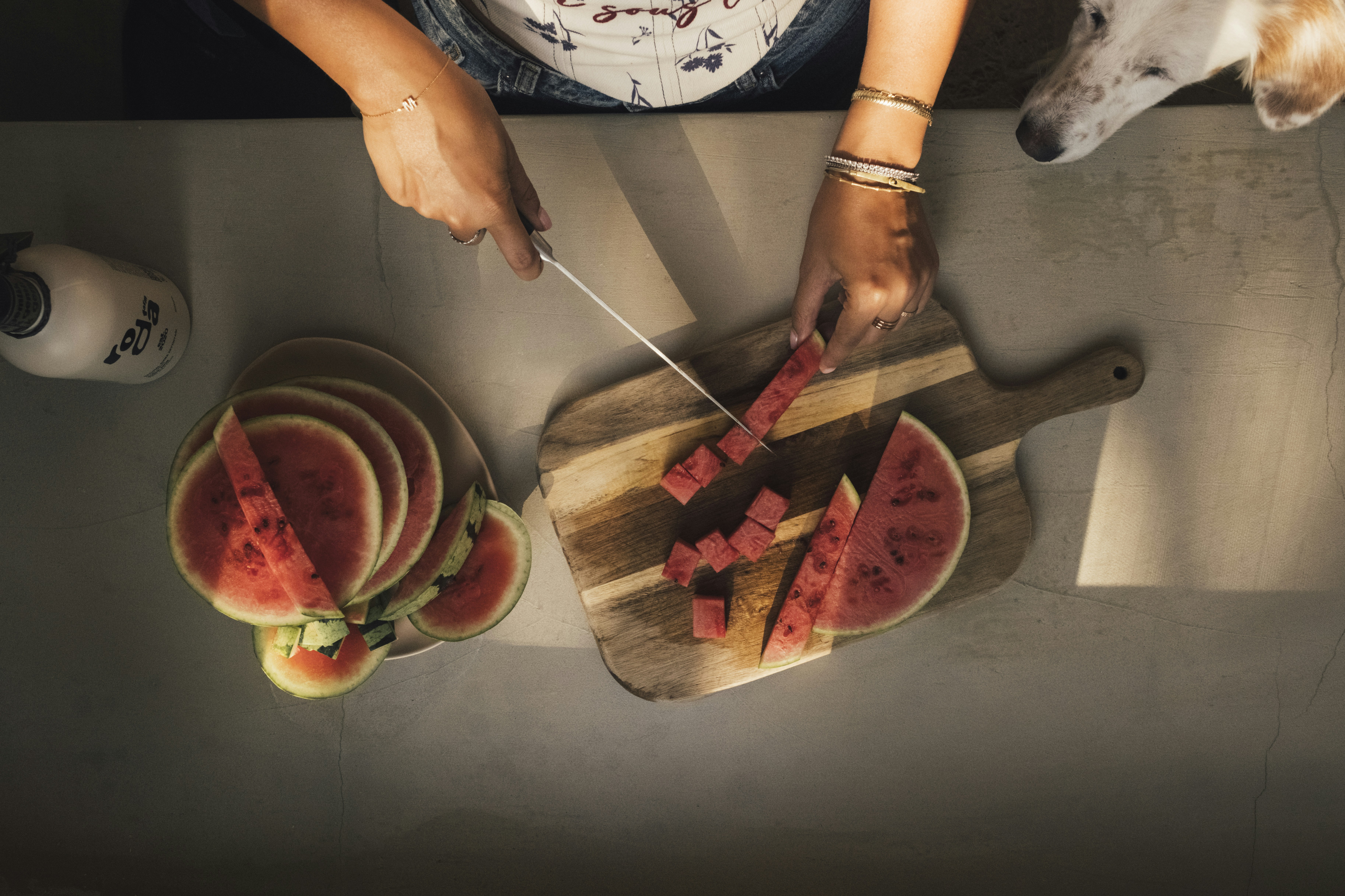 Manos cortando sandía en una tabla de cortar, relojes de perro.
