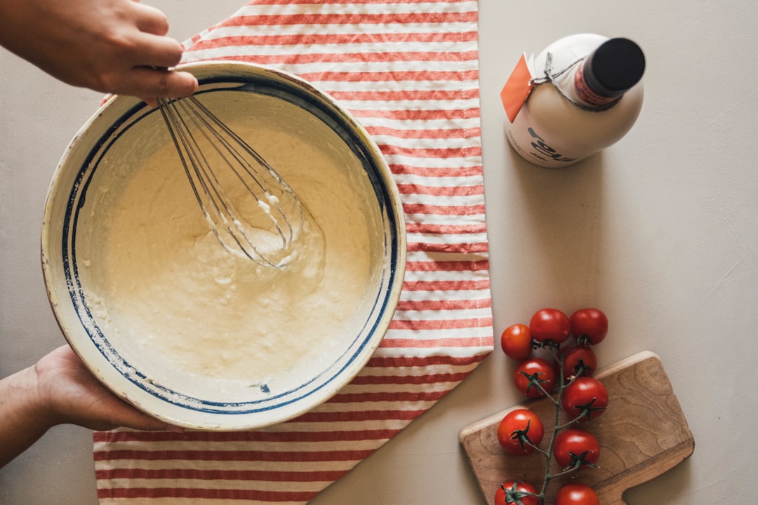 Hands whisking batter in a bowl with tomatoes nearby