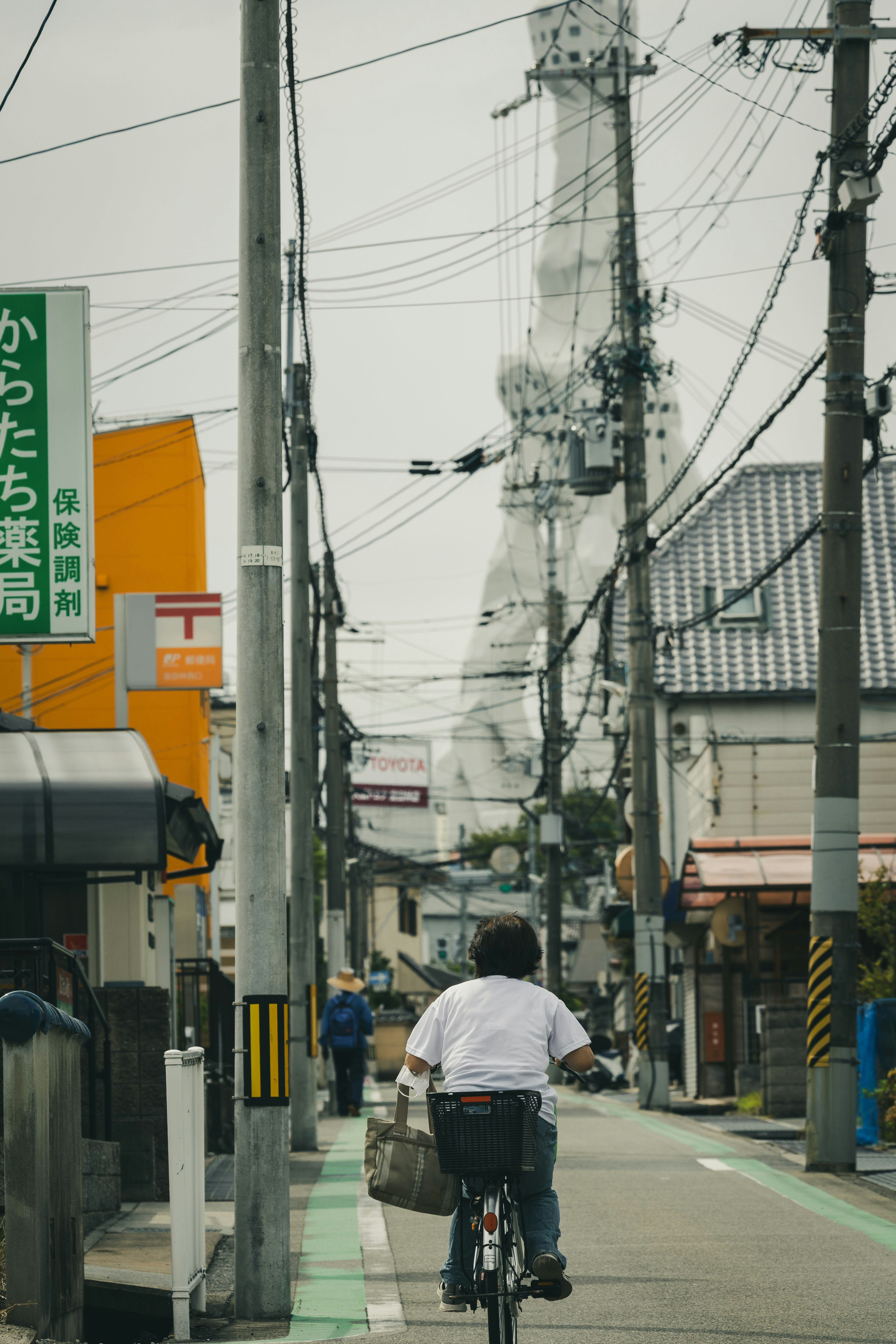 Person rides bicycle down street with power lines.