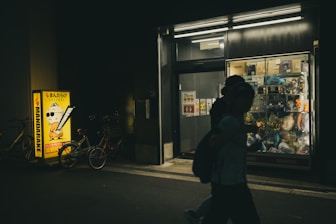 Person walks past illuminated store at night.