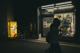 Person walks past illuminated store at night.