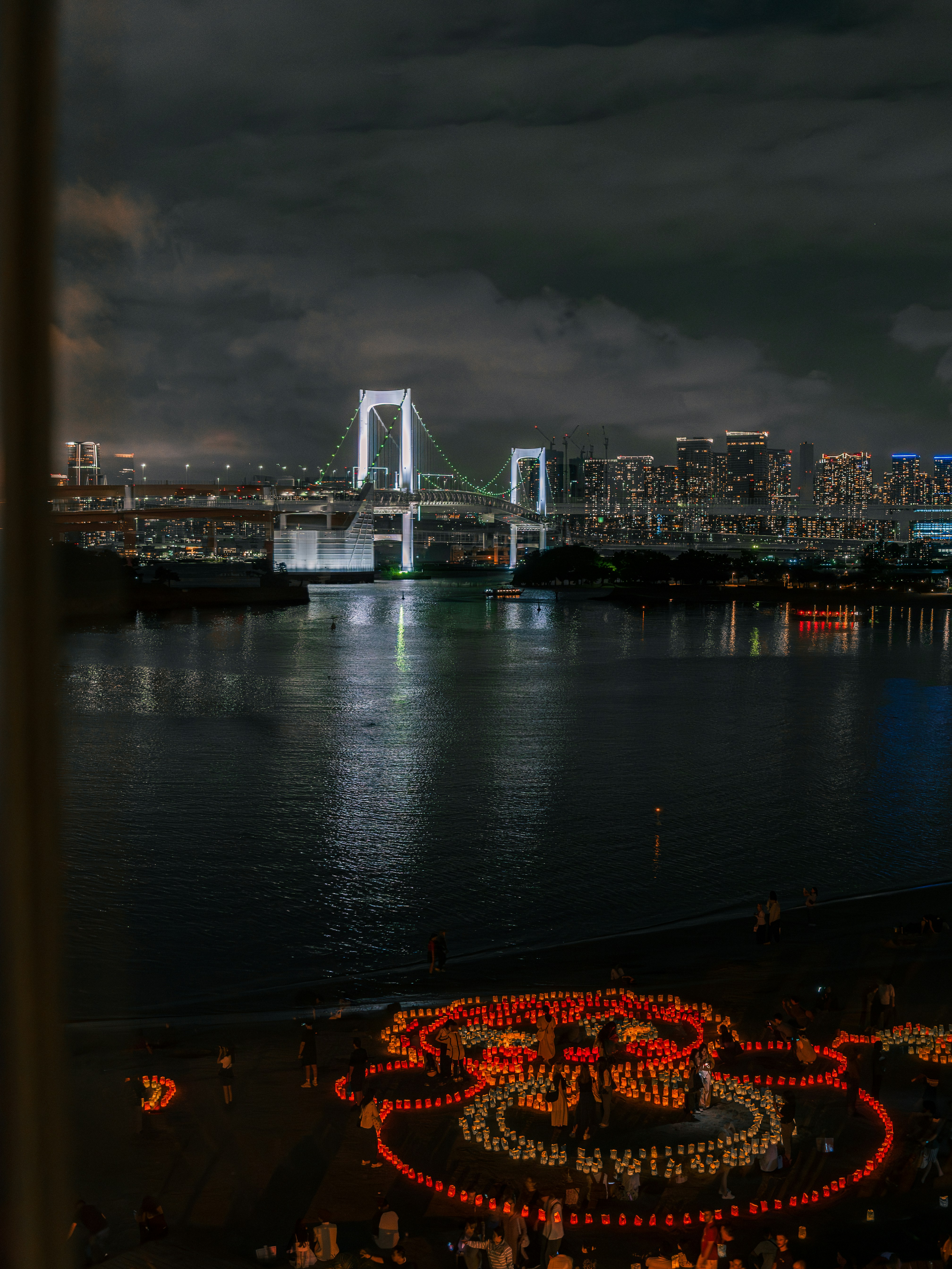 Illuminated bridge over water with city skyline at night.