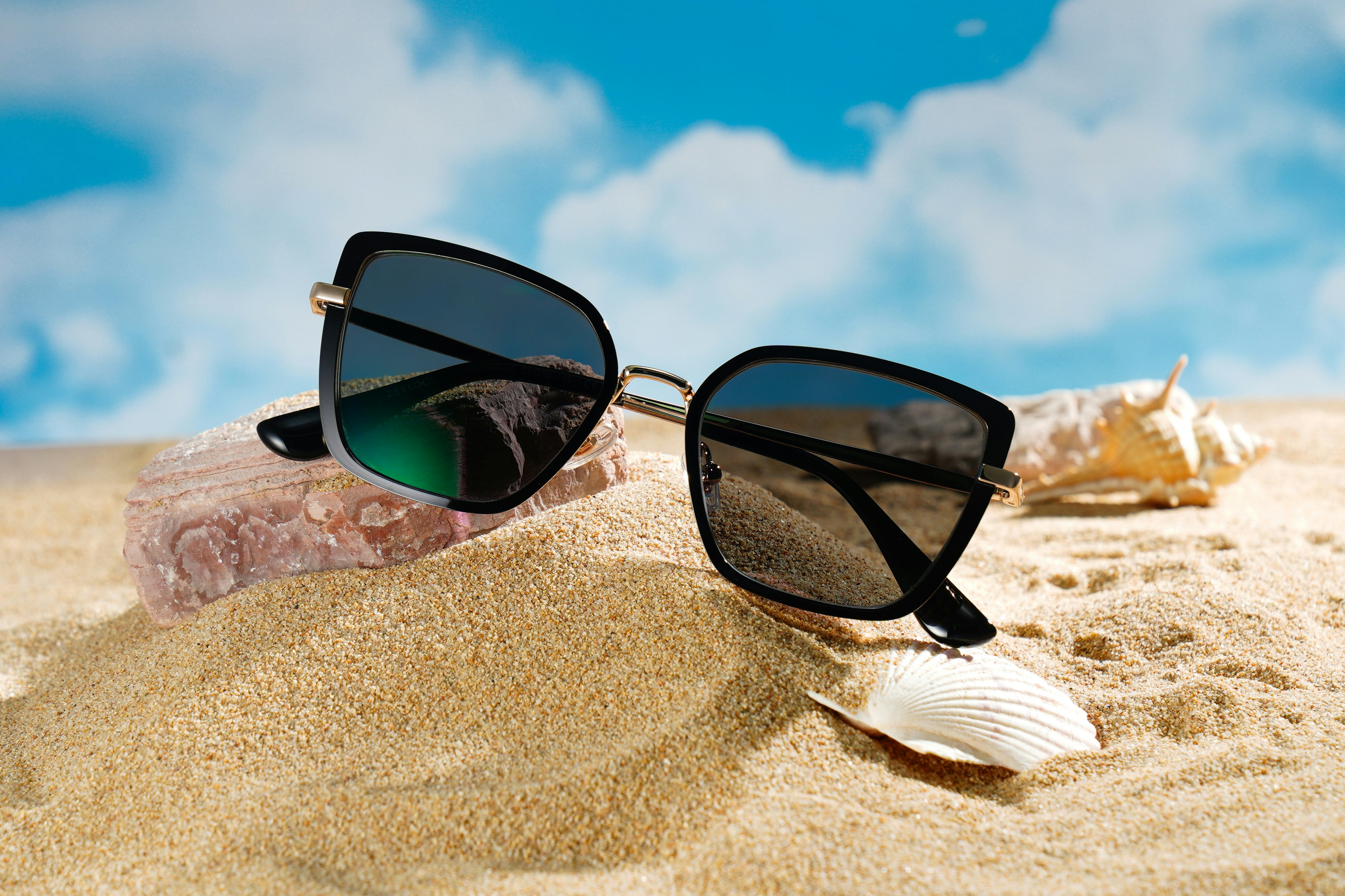 Stylish sunglasses resting on a sandy beach with shells.