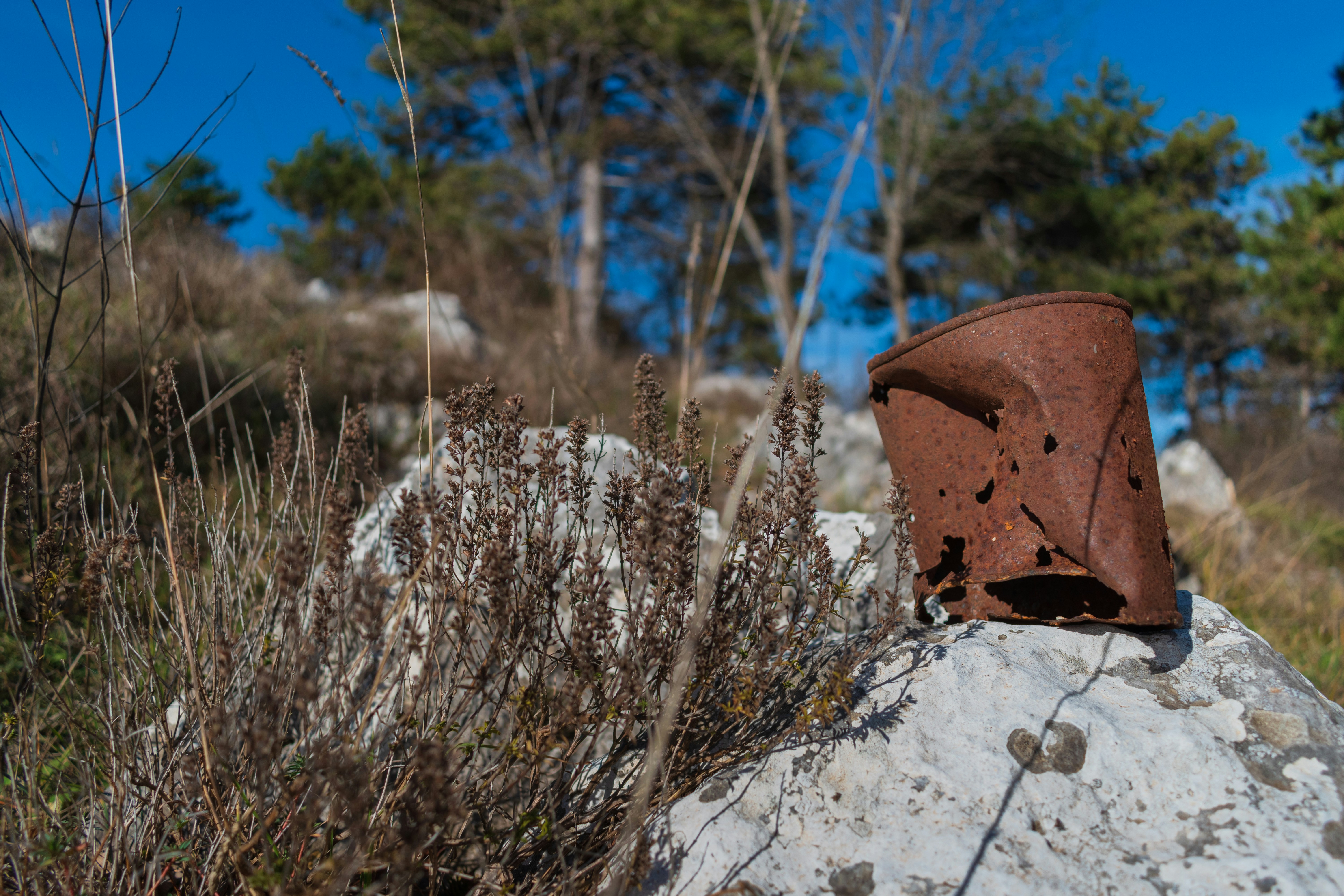 A rusty can sits on a rock outdoors.