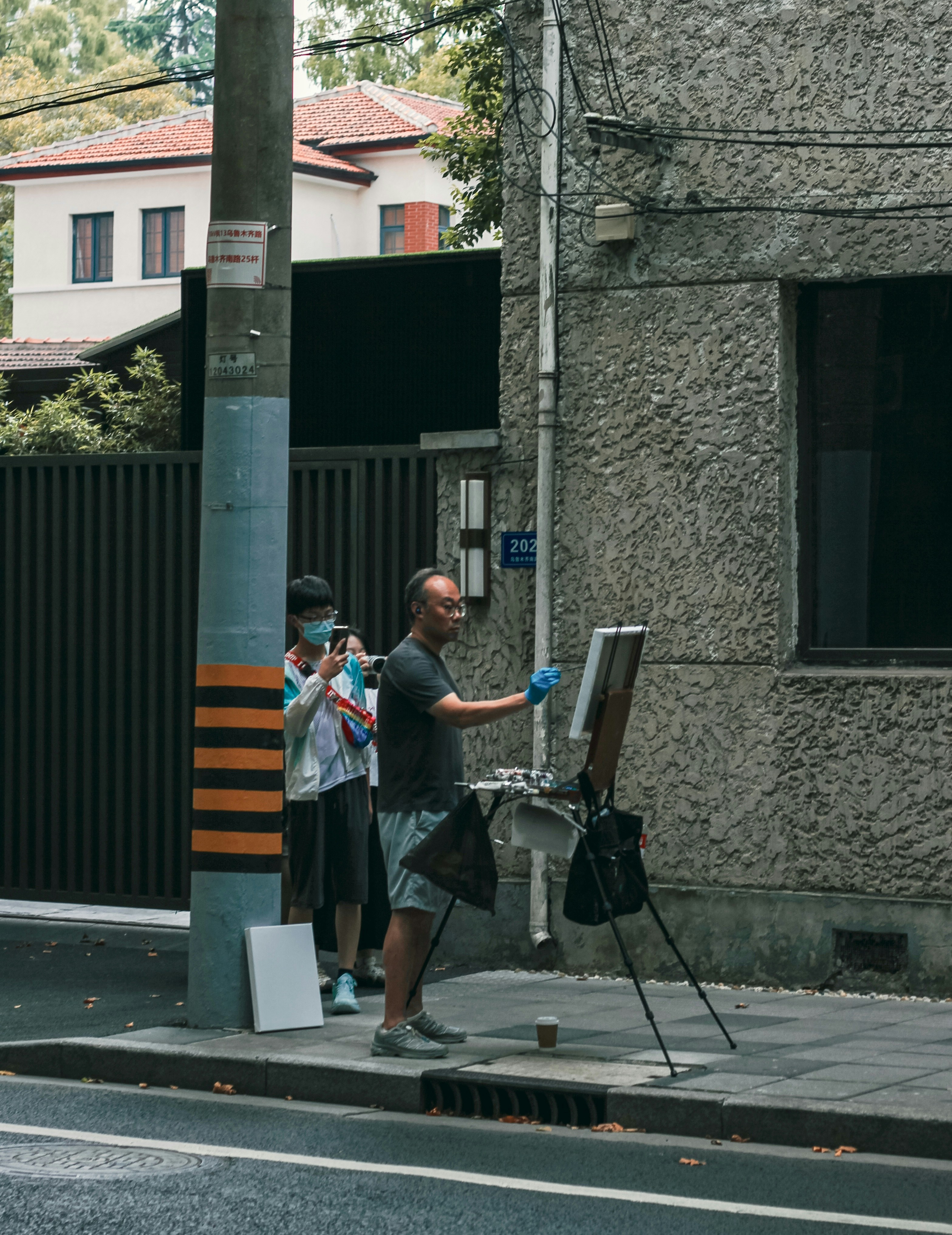 Man paints on easel on sidewalk with helper