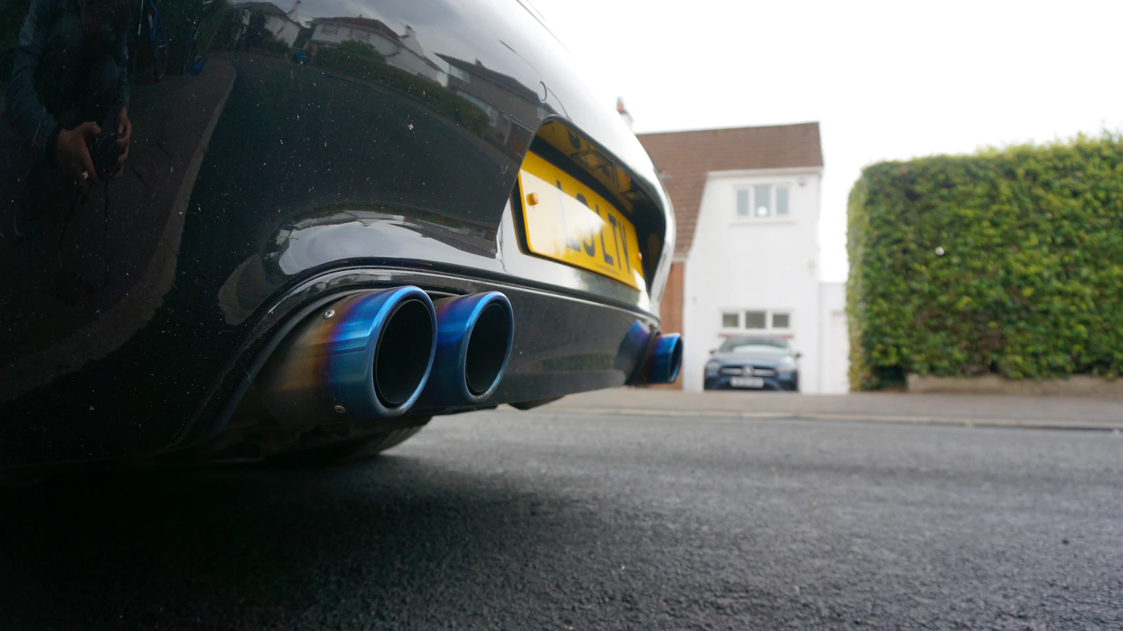 Low-angle view of a car's rear exhaust tips at road level, where an exhaust leak is usually heard first.