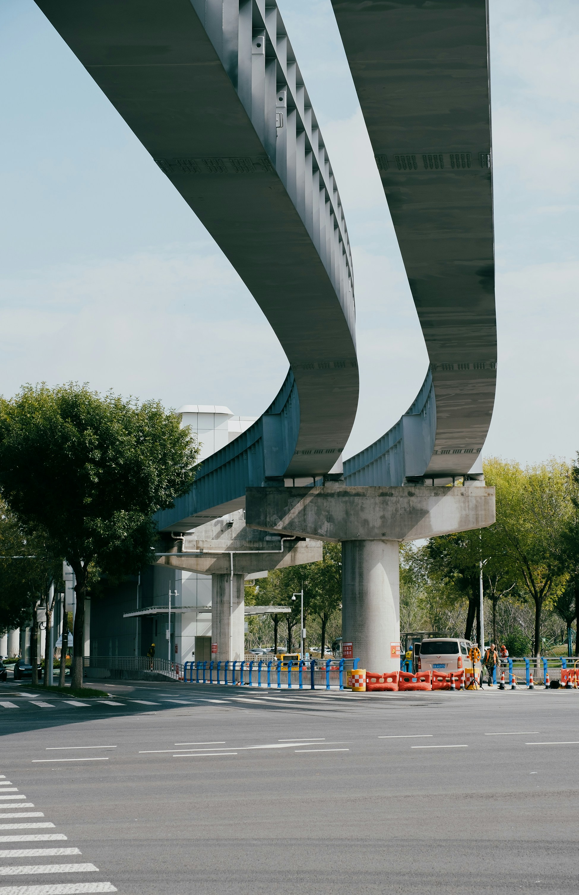 Elevated train tracks curve over a street with trees.