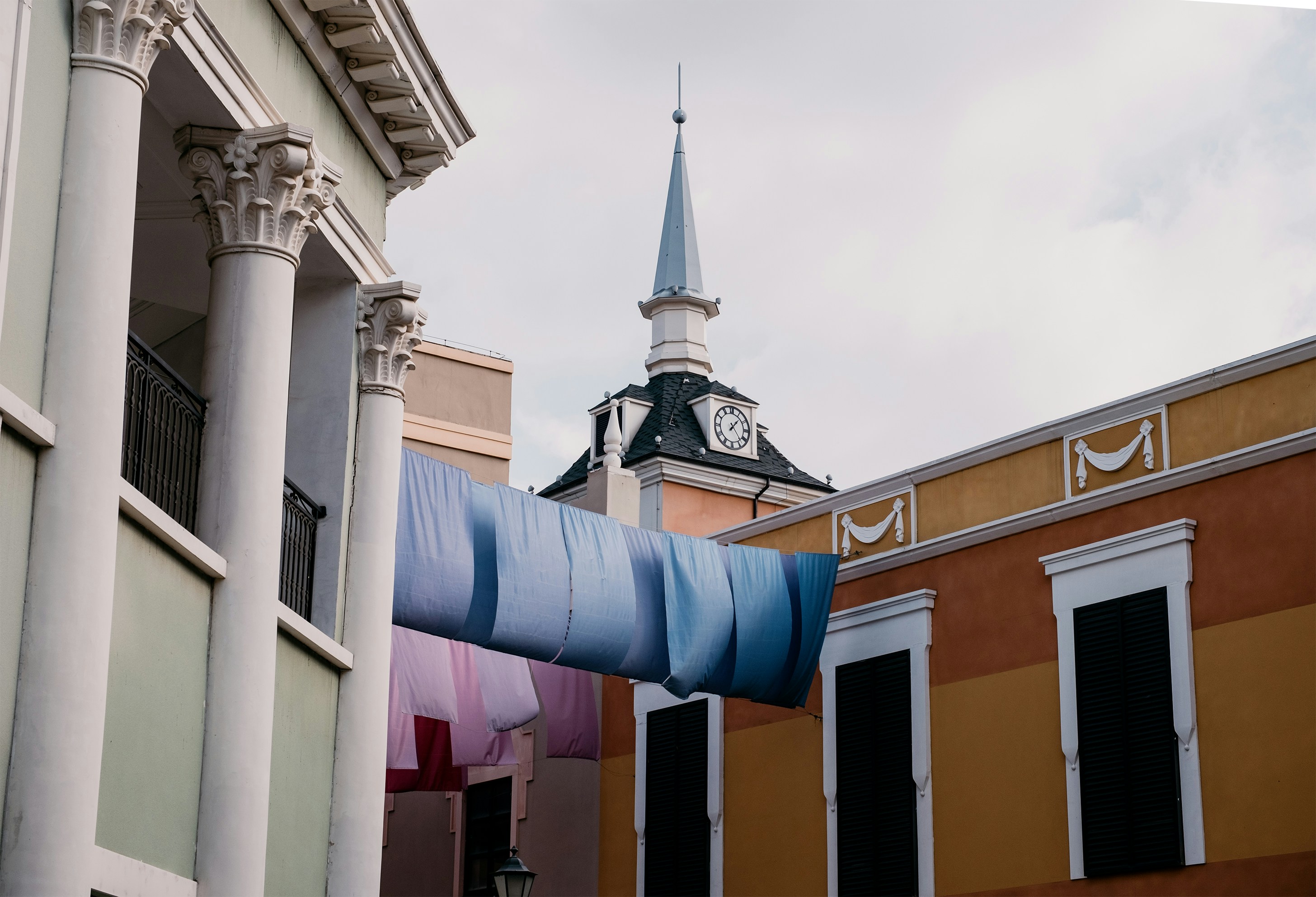 Blue fabric hangs between colorful buildings with spire.