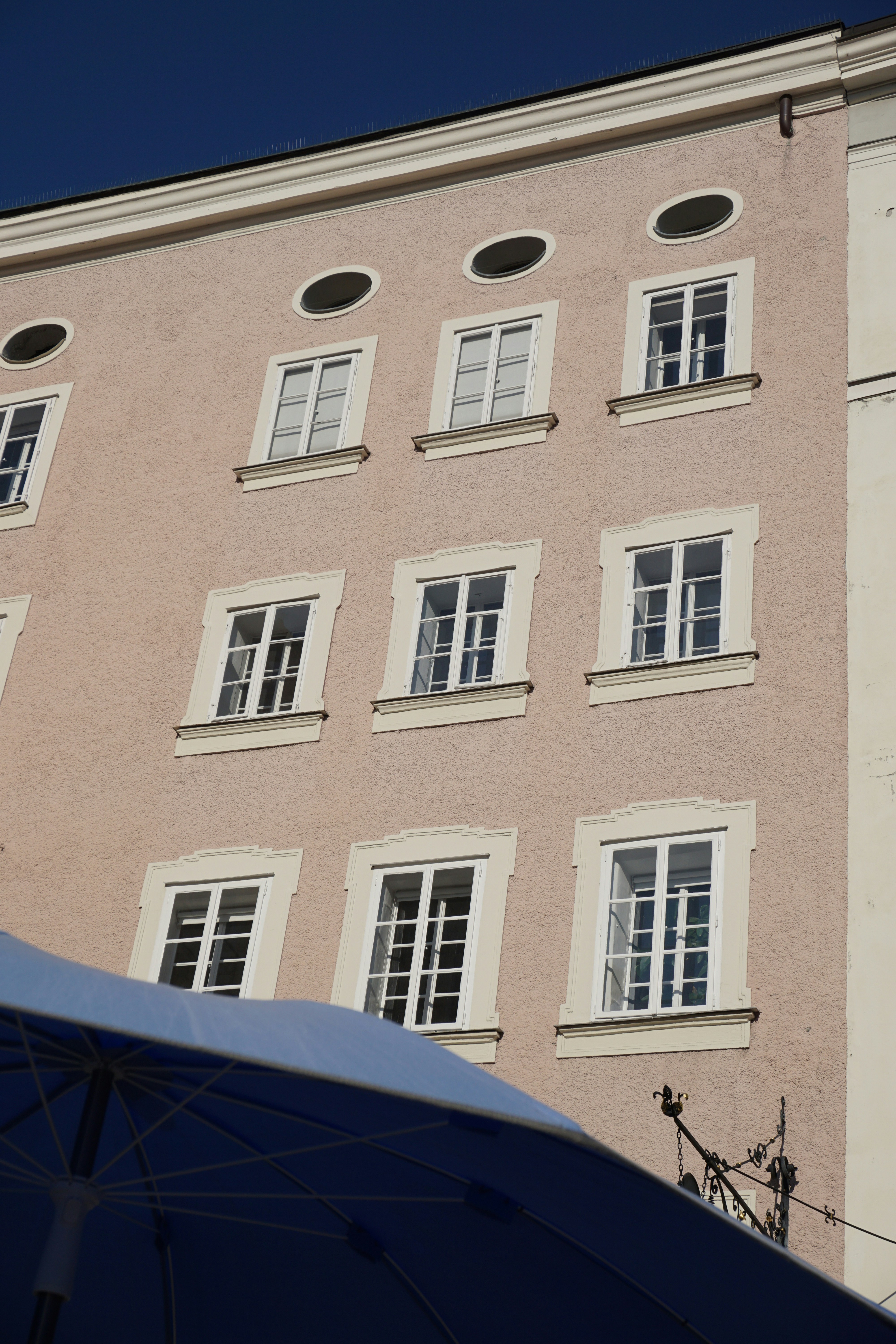 Pink building facade with nine windows and blue umbrella