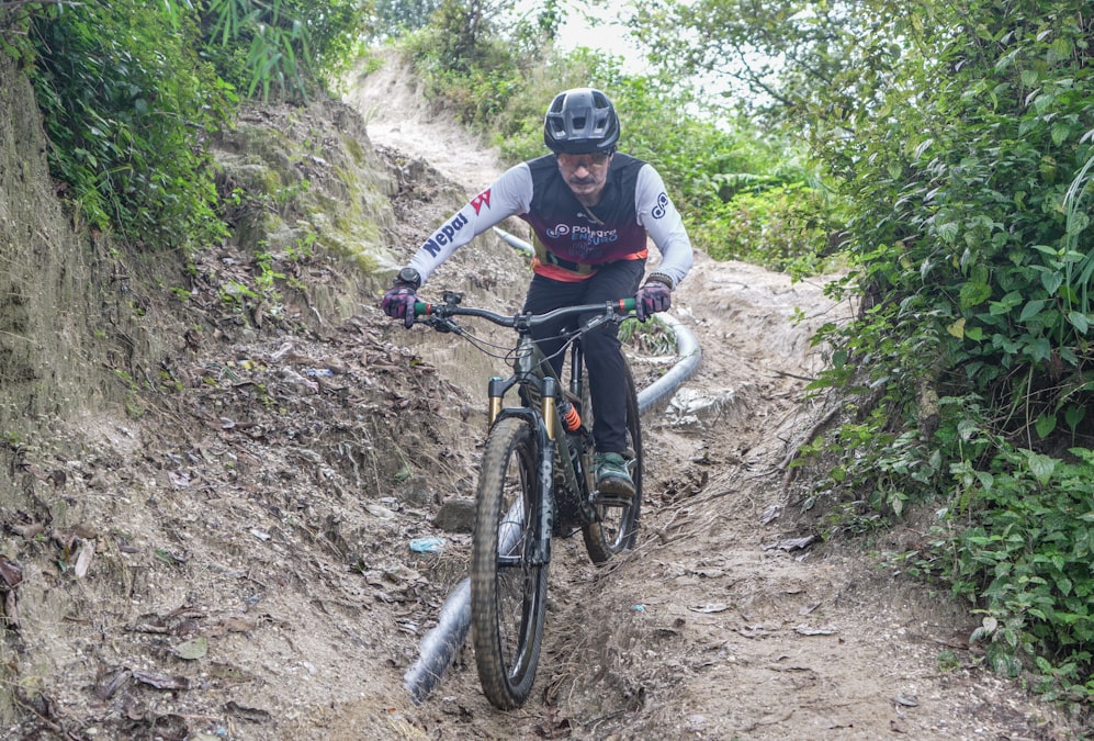 Ciclista de mountain bike descendo uma trilha de terra estreita e enlameada na mata